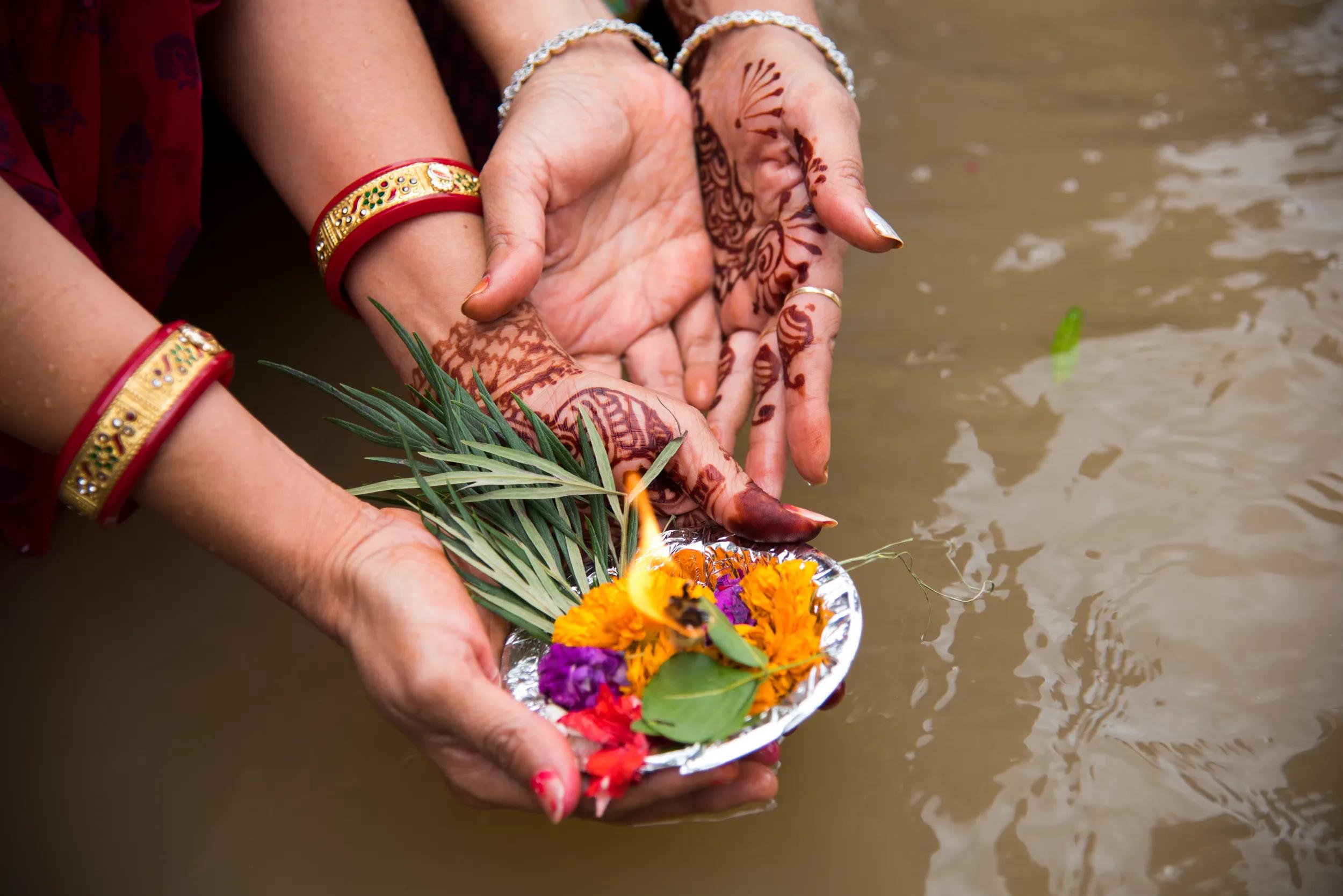 Woman hands offering light diyas (earthen lamps) to river during Kumbh Mela.