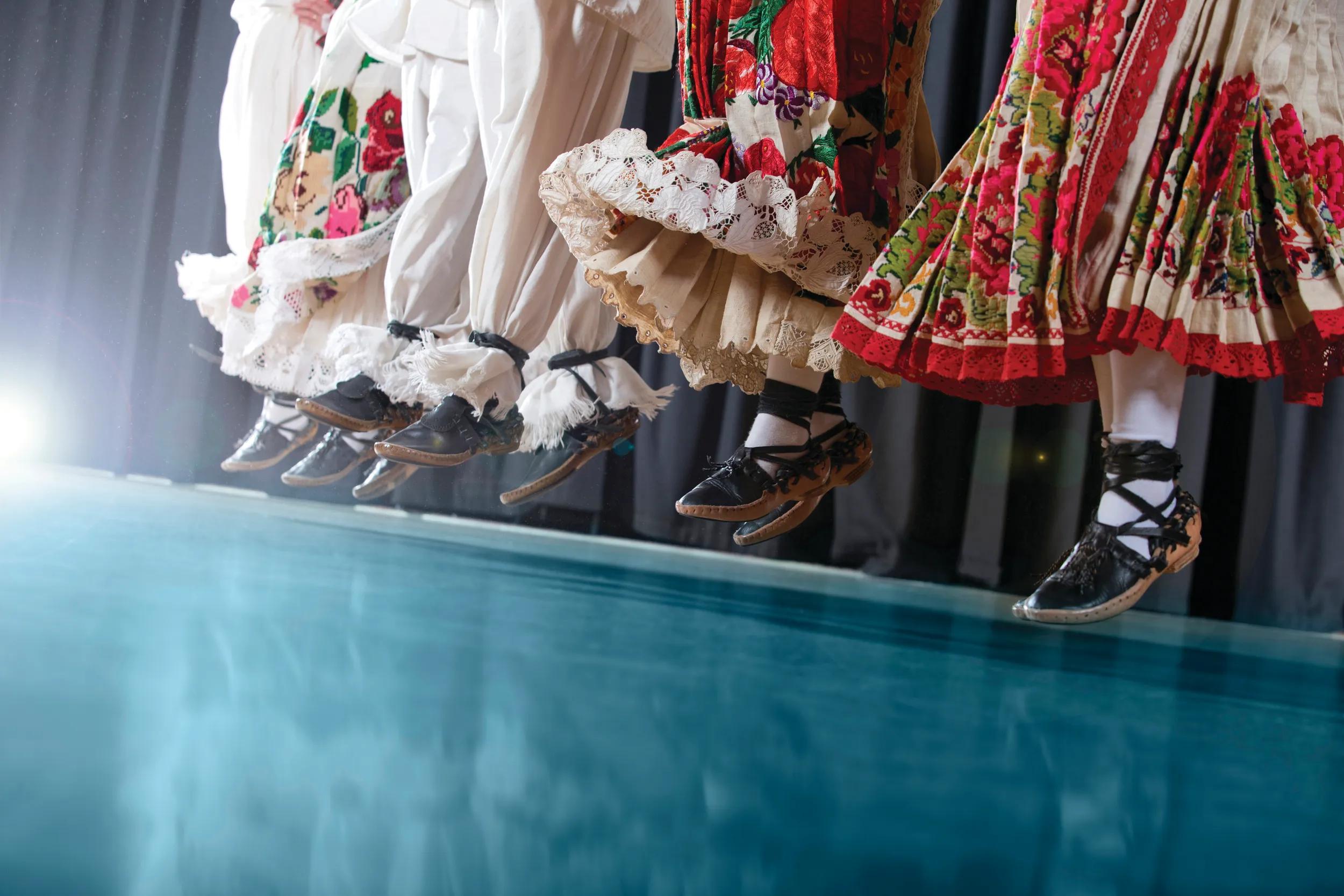 Traditional Croatian Folklore Dancers in action, short depth of field, reflection on blue floor, slight flair of light and dusk particles from clothes showing on dark areas