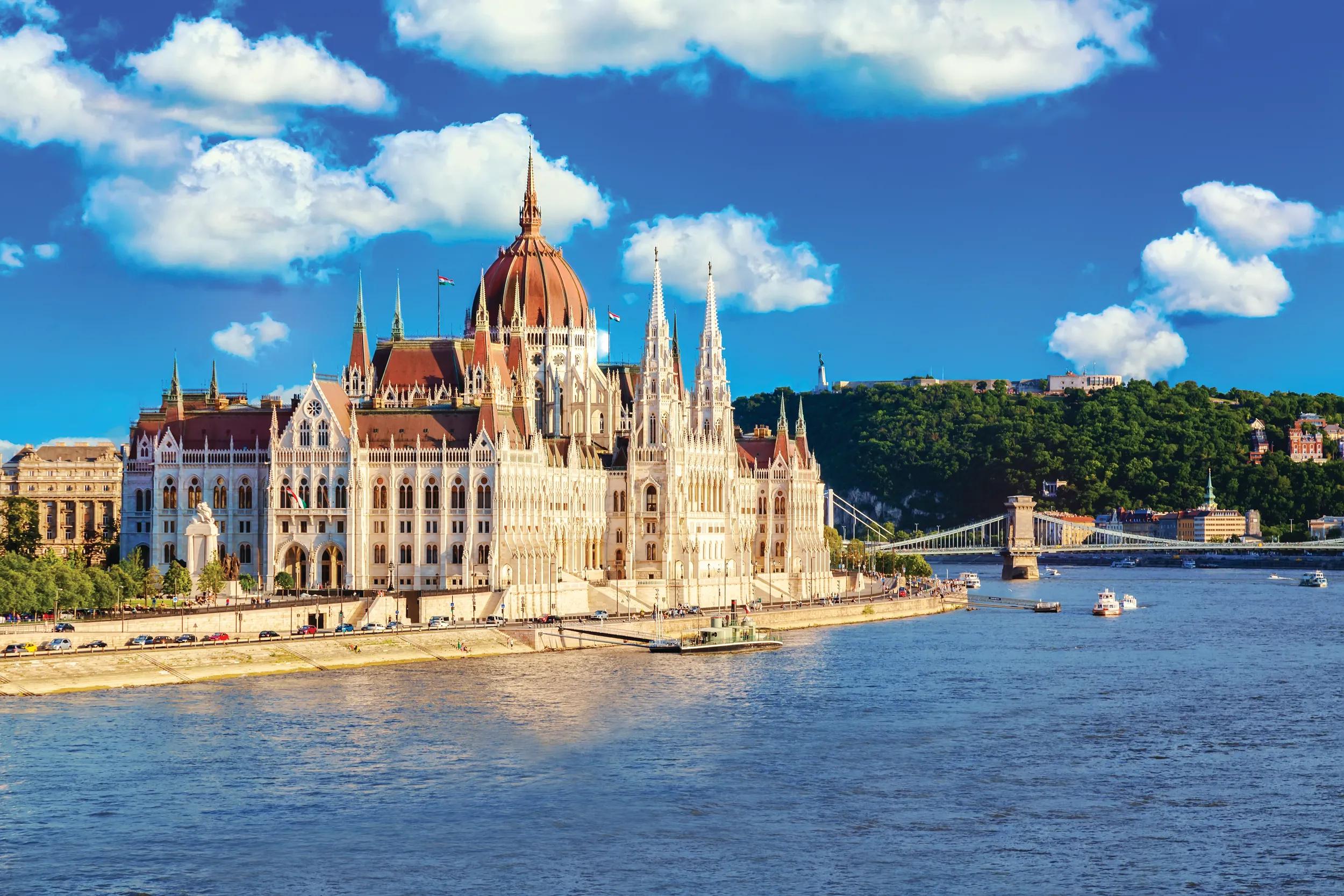 Parliament and riverside in Budapest Hungary with sightseeing ships during summer sunny day with blue sky and clouds. Travel and european tourism concept