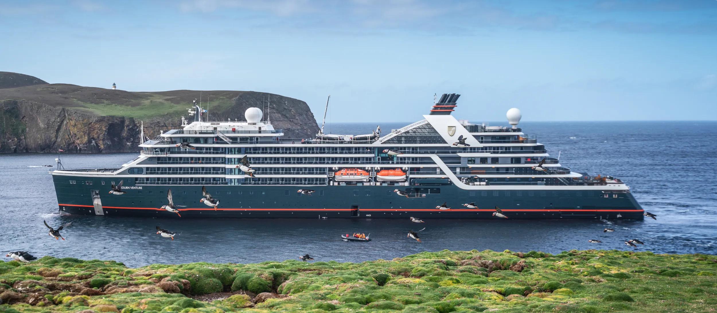 Seabourn Venture Ship in Fair Isles Scotland with Puffin Birds in focus flying in foreground.