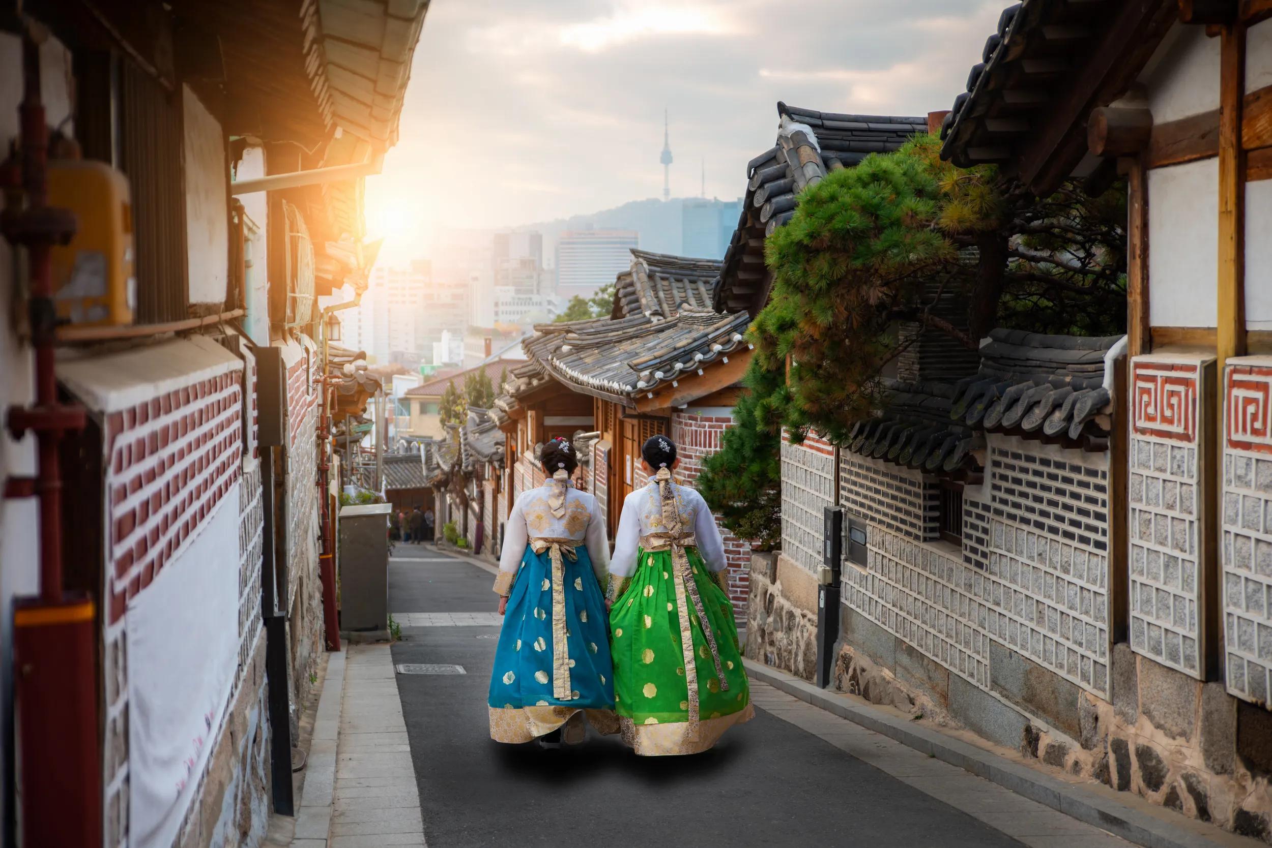 Back of two woman wearing hanbok walking through the traditional style houses of Bukchon Hanok Village in Seoul, South Korea.