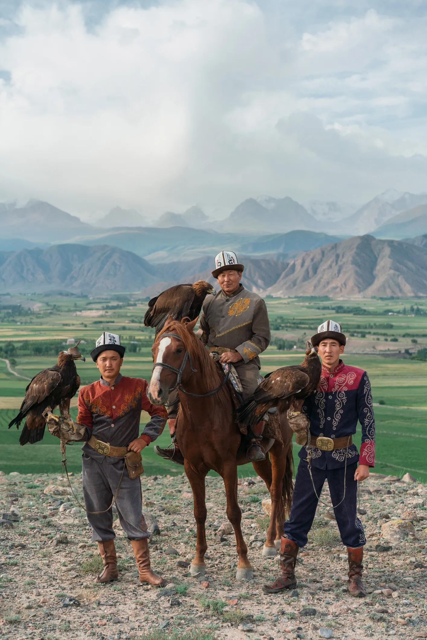 Three eagle hunters, one of them on horse, in steppe in Kyrgyzstan