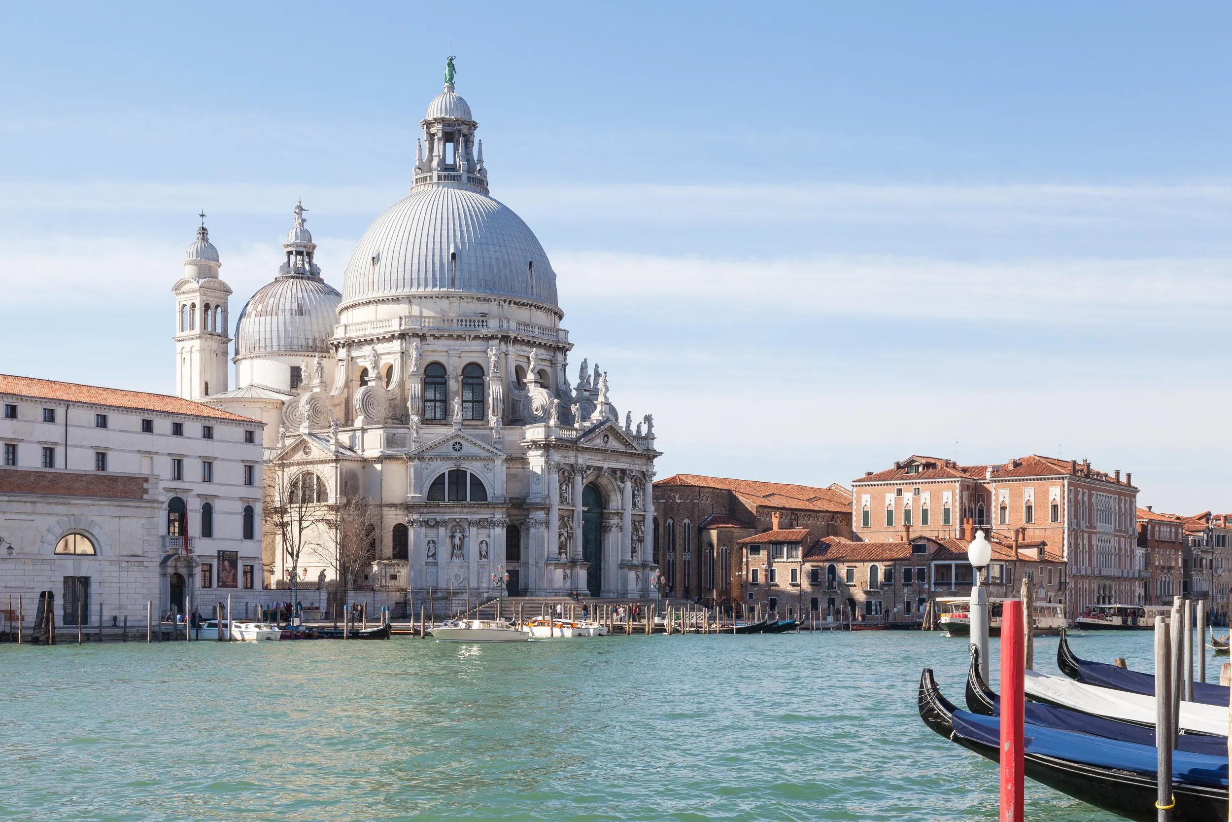 View of Basilica di Santa Maria della Salute in  Dorsoduro in  early morning light across the Grand Canal, Venice, Italy with gondolas moored to the side in a travel and tourism concept
