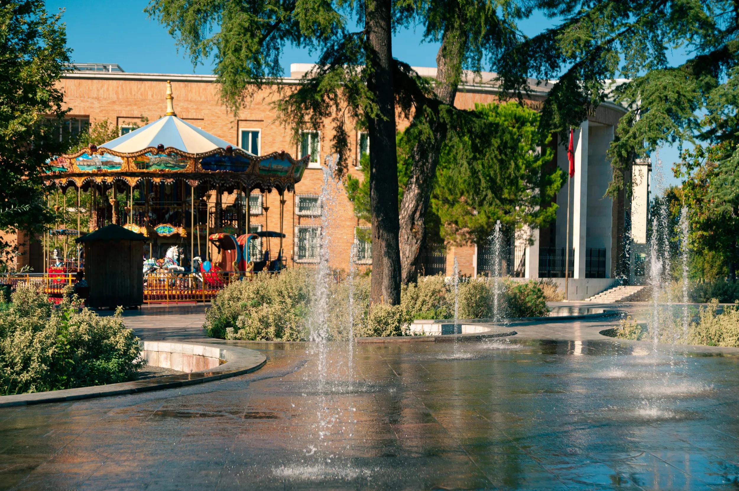 September 26th, 2021 - Tirana, Albania: View of a carousel (merry go round), water fountain on the Skanderbeg Square in downtown Tirana, against a sunny clear blue sky.