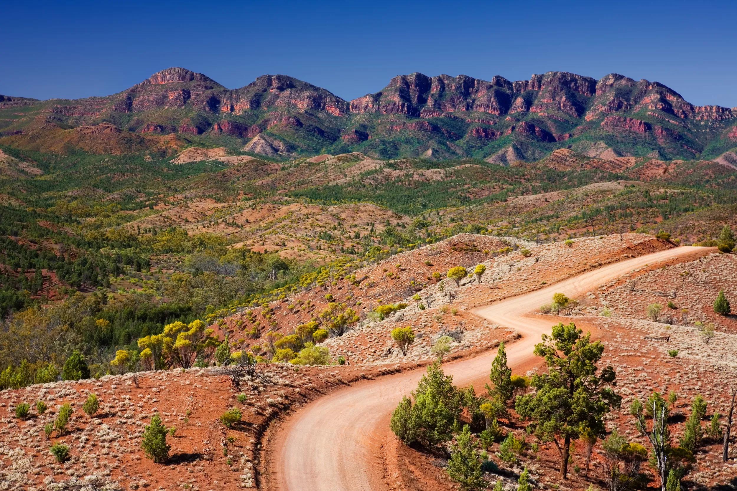 View of the mountain ranges and the valley with a winding dirt road from Razorback Lookout in Flinders Ranges National Park in South Australia outback