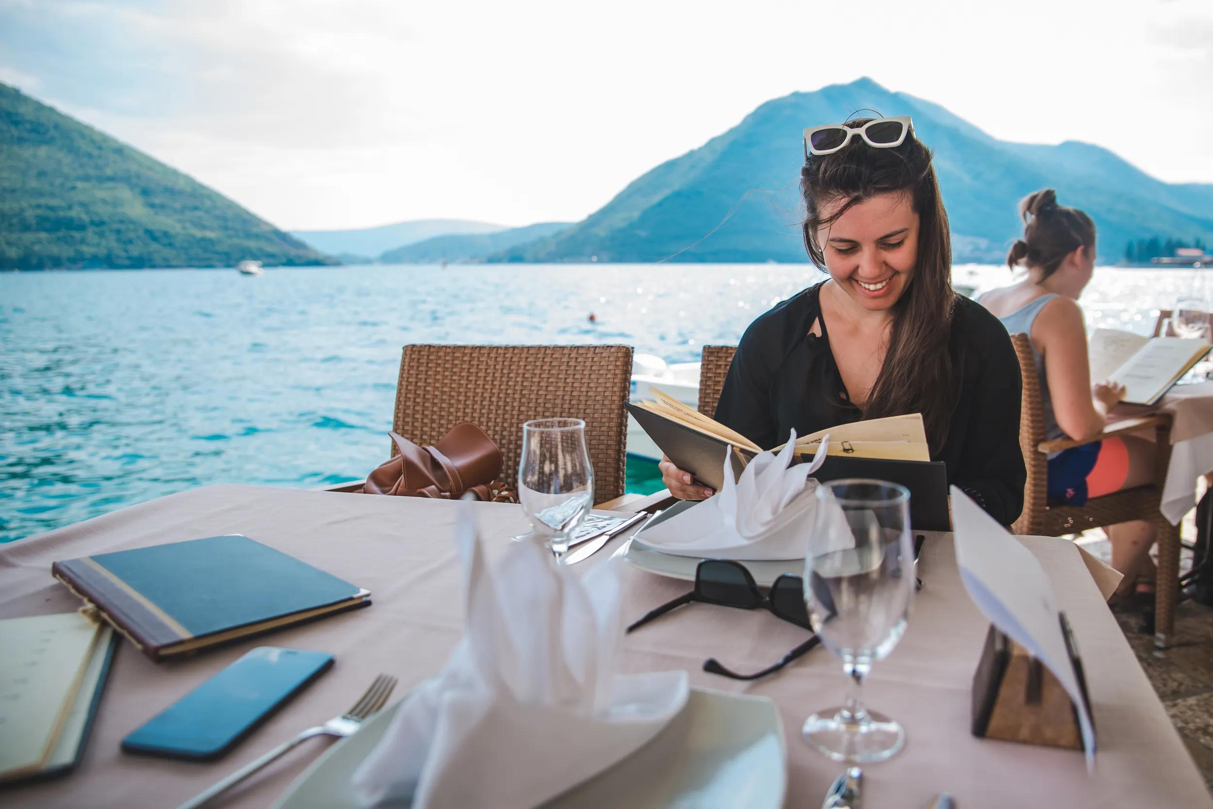 young pretty woman sitting in restaurant at seaside with mountains on background. summer vacation