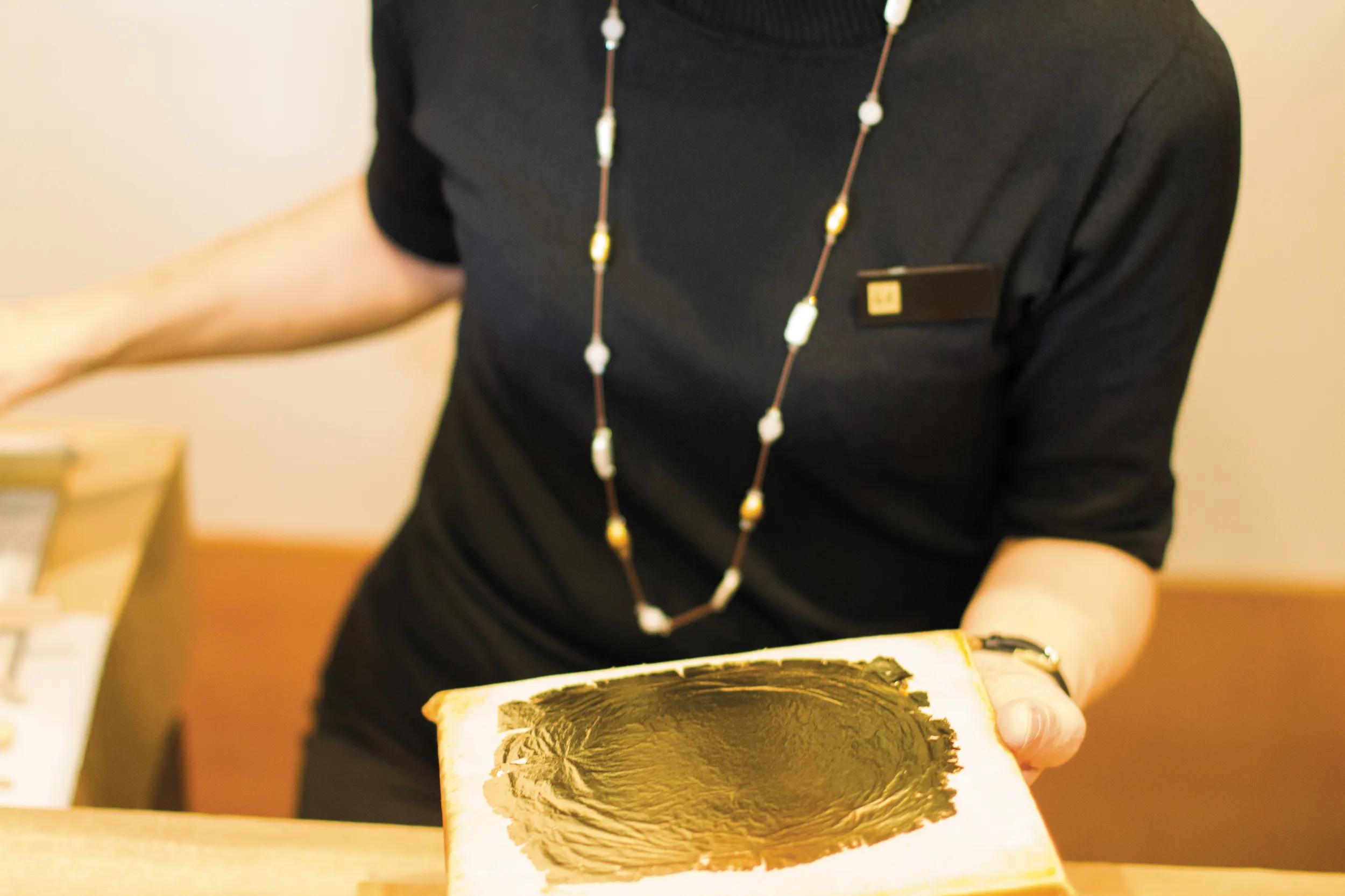A clerk holding up a sheet of Kanazawa wagasa, or Kanazawa gold leaf, an extremely thin sheet of gold used to cover other objects to give them a golden appearance.