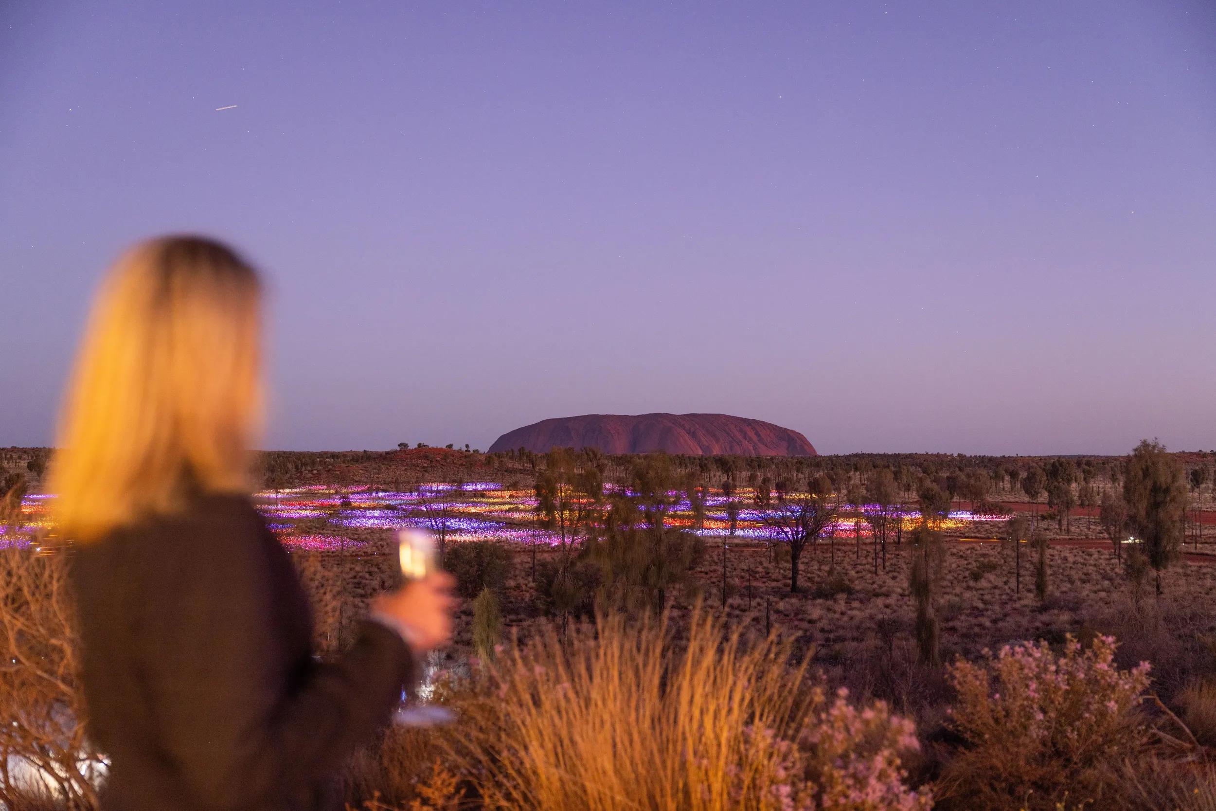 As darkness falls and Uluru is thrown into silhouette, Field of Light illuminates. As far as the eye can see gentle rhythms of colour light up the desert.The critically acclaimed Field of Light Uluru by the internationally celebrated artist Bruce Munro is on display and due to popular demand, has now been extended indefinitely.The exhibition, aptly named Tili Wiru Tjuta Nyakutjaku or ‘looking at lots of beautiful lights?? in local Pitjantjatjara is Munro??s largest work to date. Overwhelming in size, covering more than seven football fields, it invites immersion in its fantasy garden of 50,000 spindles of light, the stems breathing and swaying through a sympathetic desert spectrum of ochre, deep violet, blue and gentle white.