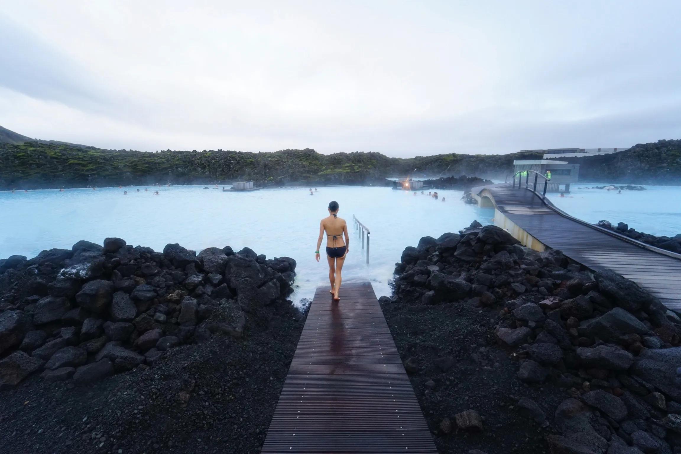 A woman in a bikini swimsuit walking down the path towards the lagaoon at the Blue Lagoon in Iceland.