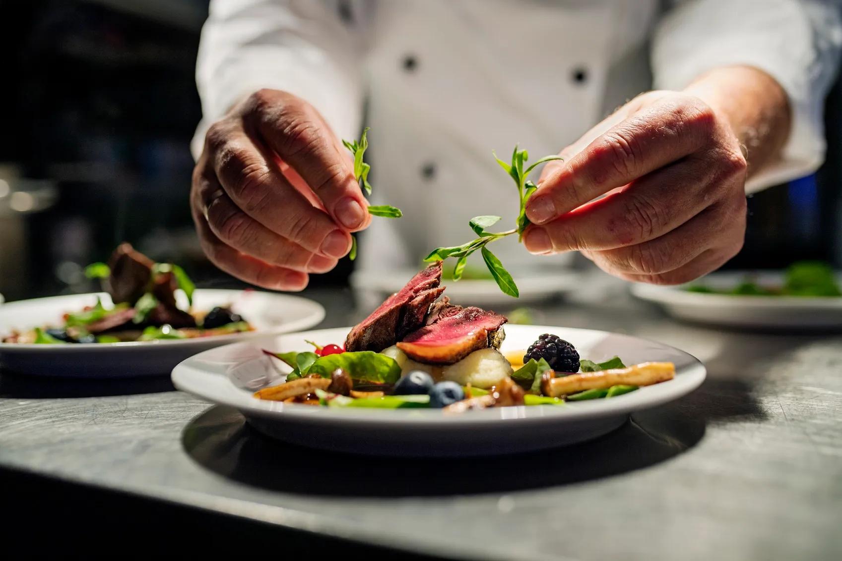 Chef adding the final flourish by adding some liquorice flavoured  parsley to the dish. The dish is, pan fried pink duck breast onto a bed of parsnip puree with seasonal autumn vegetables and berries. Colour, horizontal with some copy space, photographed on location in a restaurant on the island of Møn in Denmark.