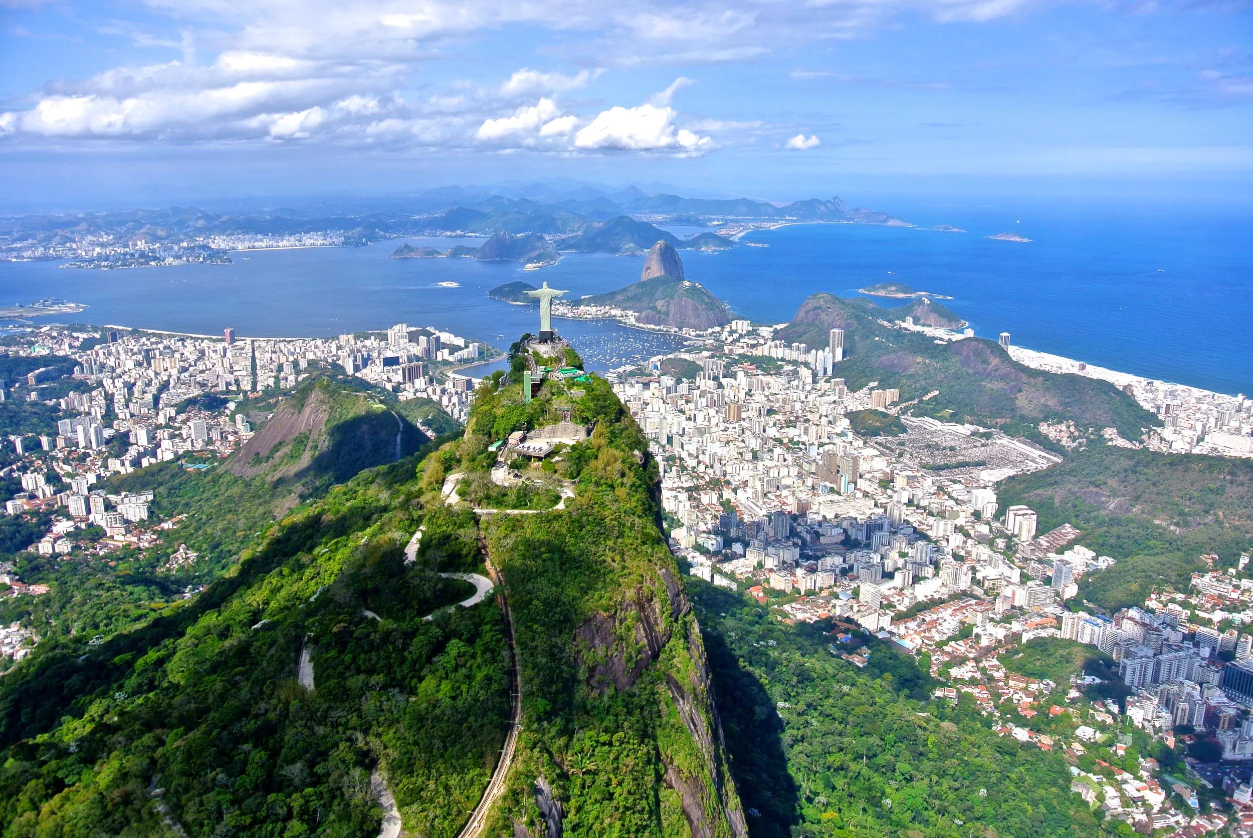 Aerial view of the Christ Redeemer overlooking Rio de Janeiro, with Sugarloaf Mountain in background.