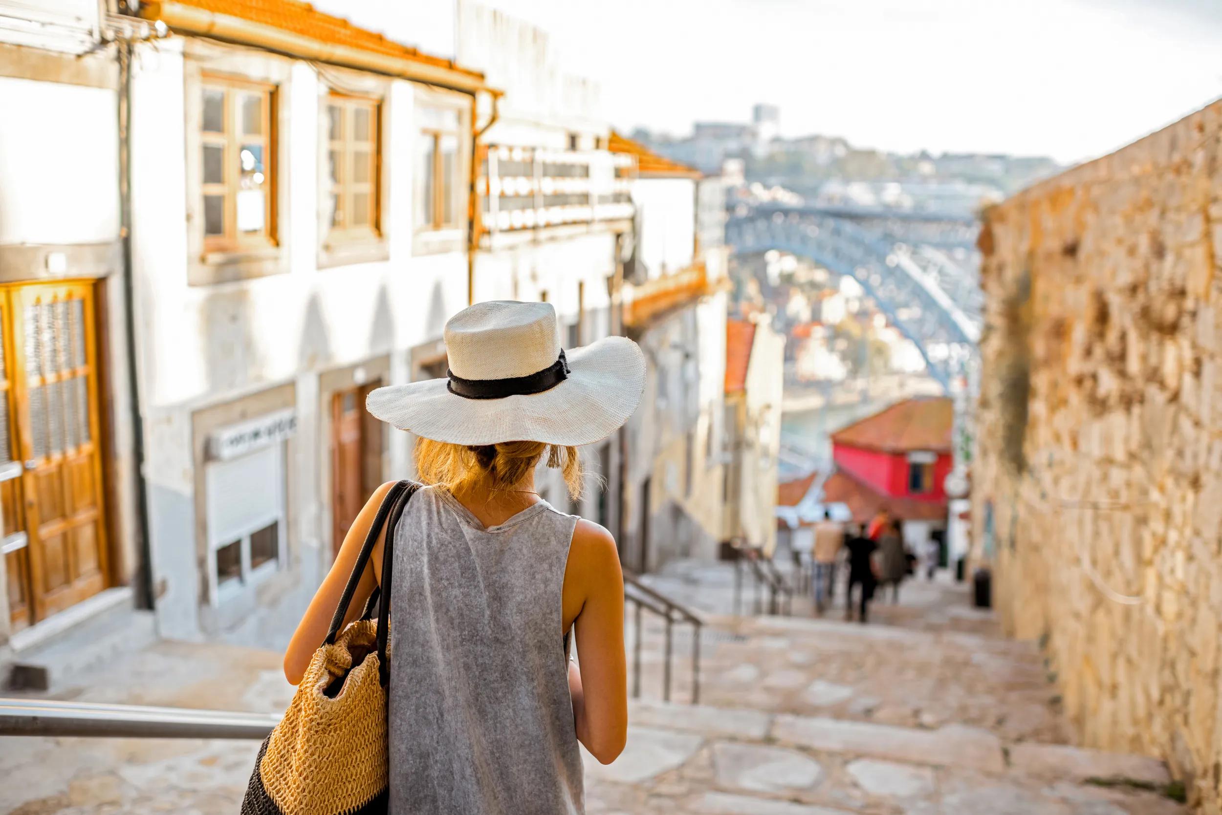 Young woman tourist walking down the stairs with famous iron bridge on the background in Porto city, Portugal