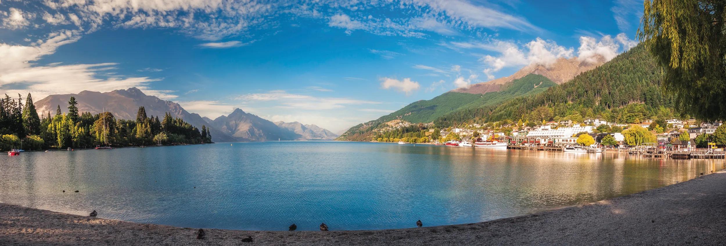 Early morning at the beach on lake Wakatipu in Queenstown, with the wharf on the right hand side and Queenstown Gardens of the left and Southern Alps in the background.