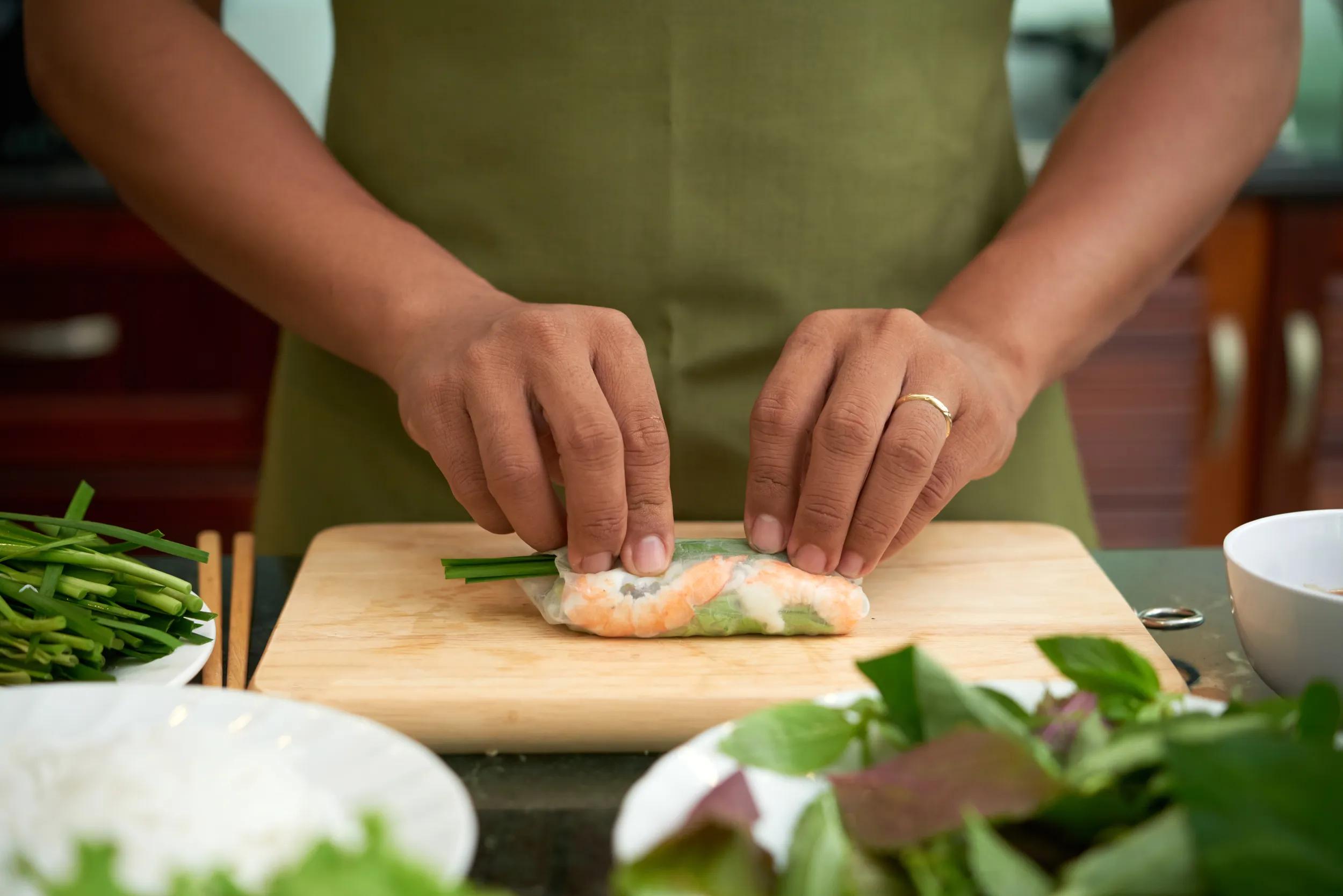 Man making traditional Asian spring rolls with shrimp and vegetables