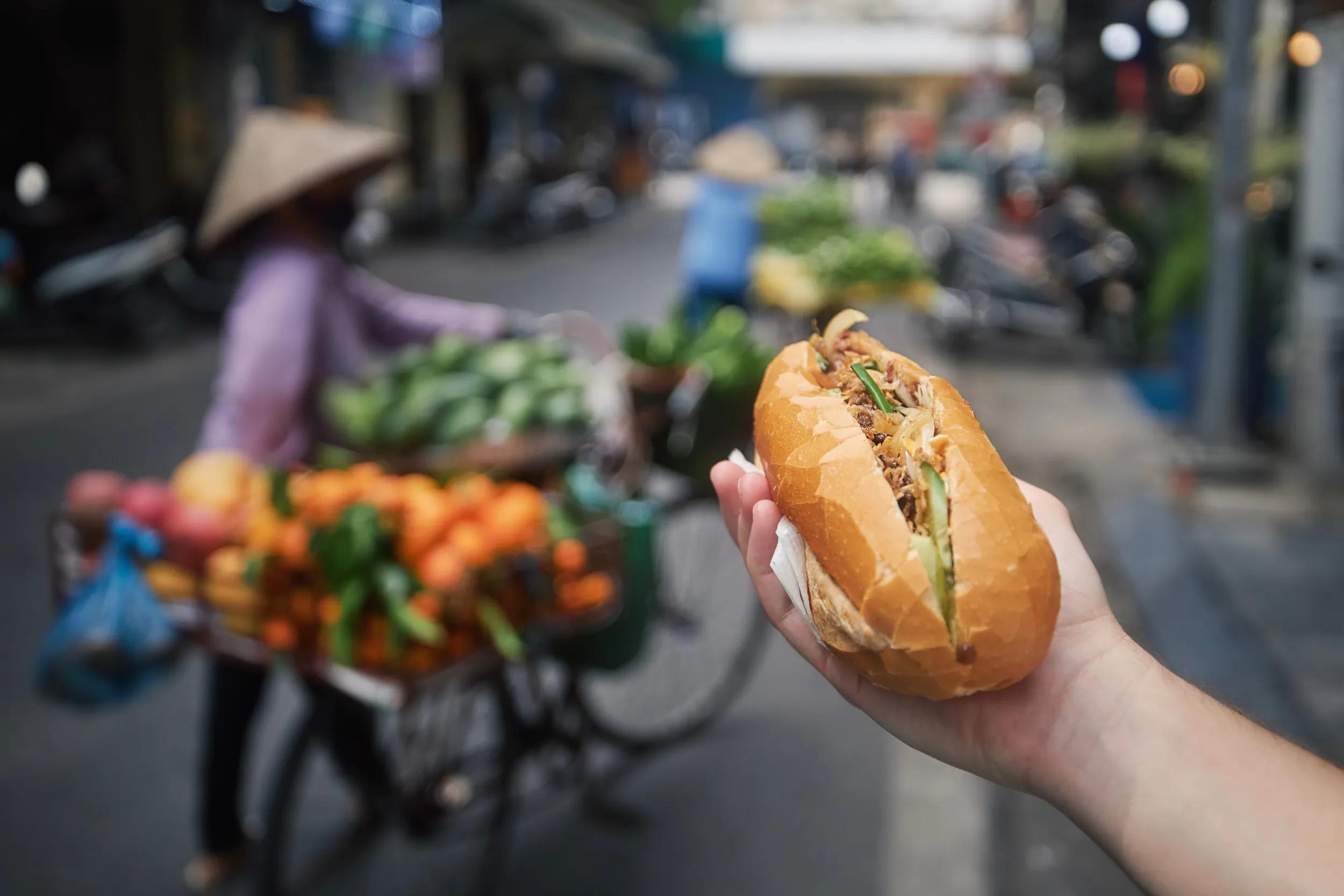Street food. Hand holding Banh Mi sandwich on street in Hanoi, Vietnam.