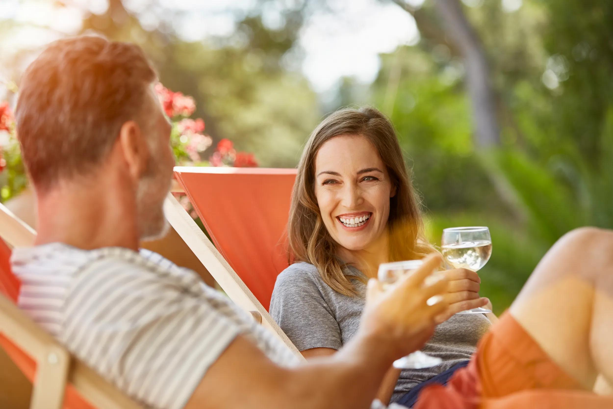Happy mature couple holding wineglasses while relaxing on deck chairs at back yard