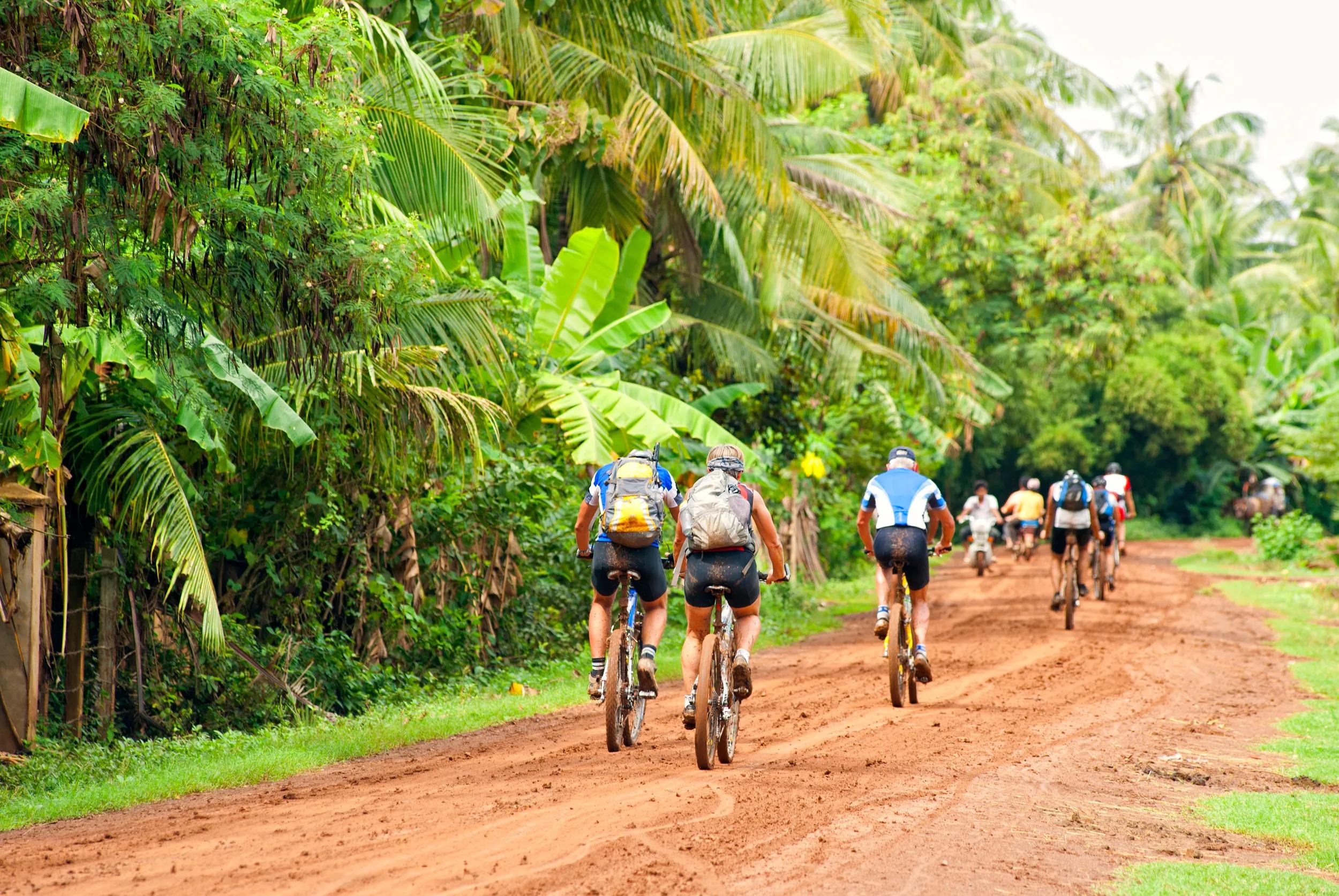 A group of mountain biker is cycling on a dirt road beside Mekong river in Northern Cambodia, close to the Laos border.