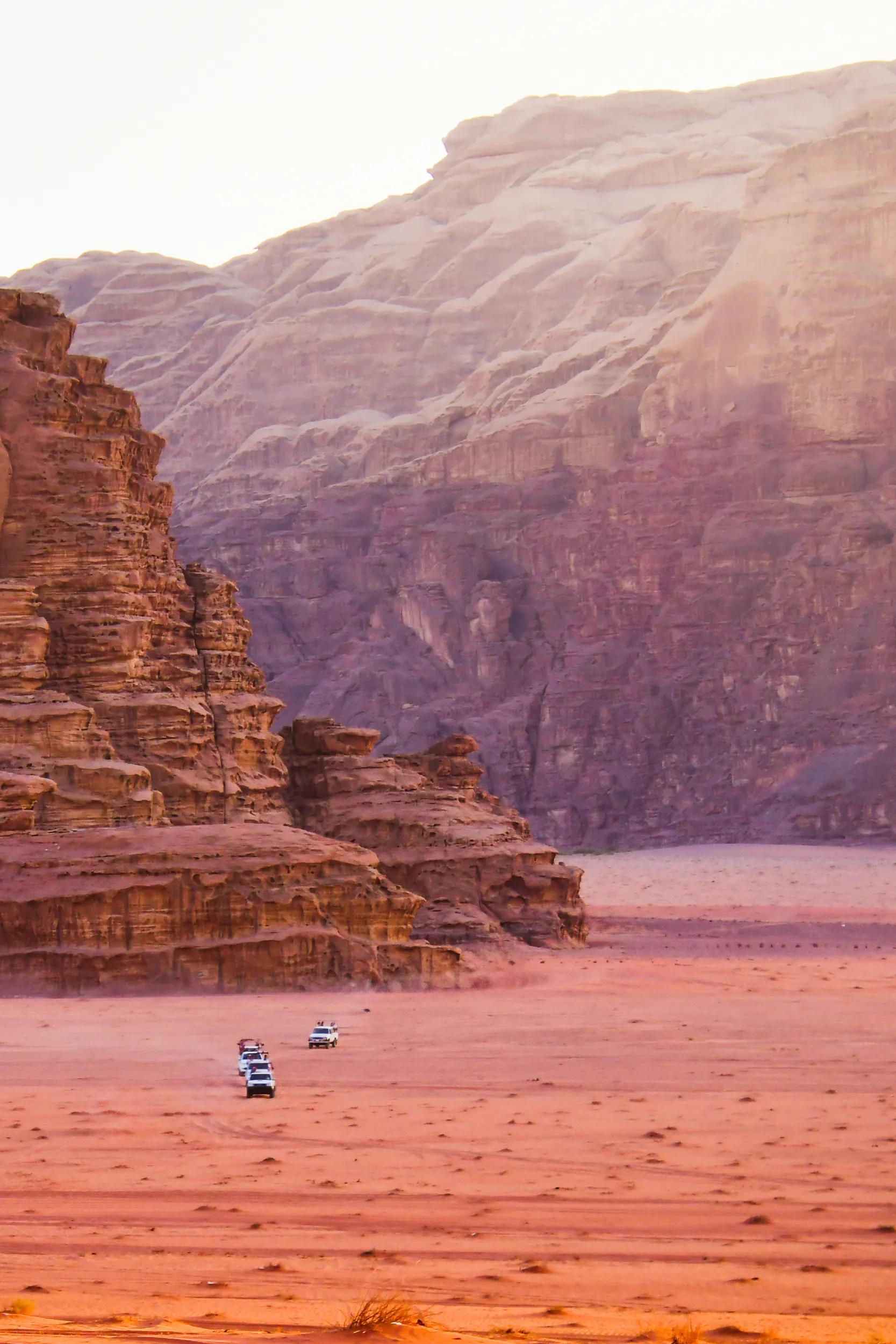 Convoy of 4x4 jeeps driving through dramatic sandstone mountains of Wadi Rum desert, concept of adventure travel, exploration, tourism, and Middle East desert experience.