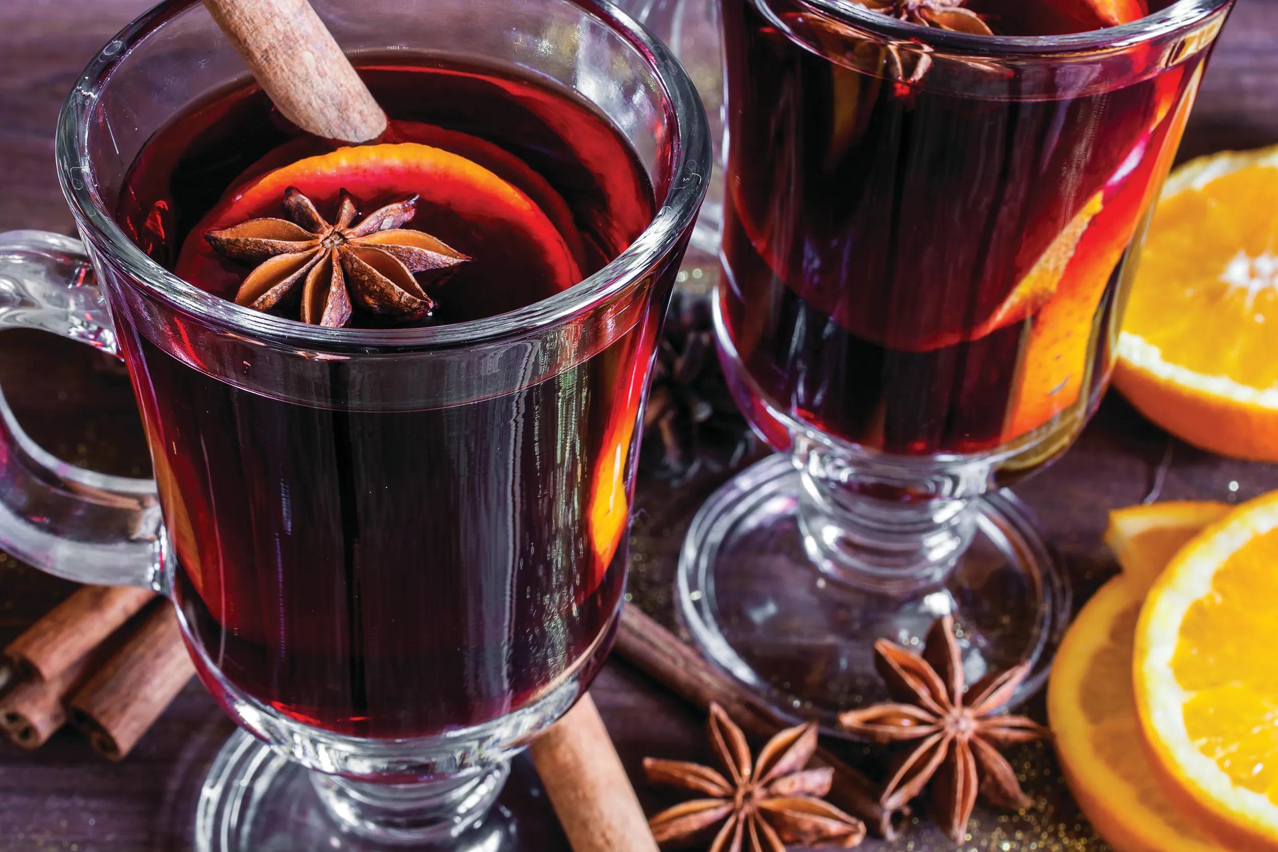 two glasses of hot mulled wine with spices and sliced orange on wooden background. close up