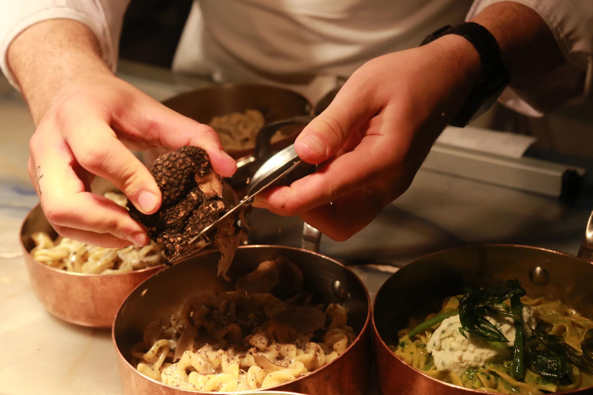 The final preparation of foods before being picked up by the servers, in an Italian restaurant in Paris.  The chef is grating truffles on to a pasta dish.