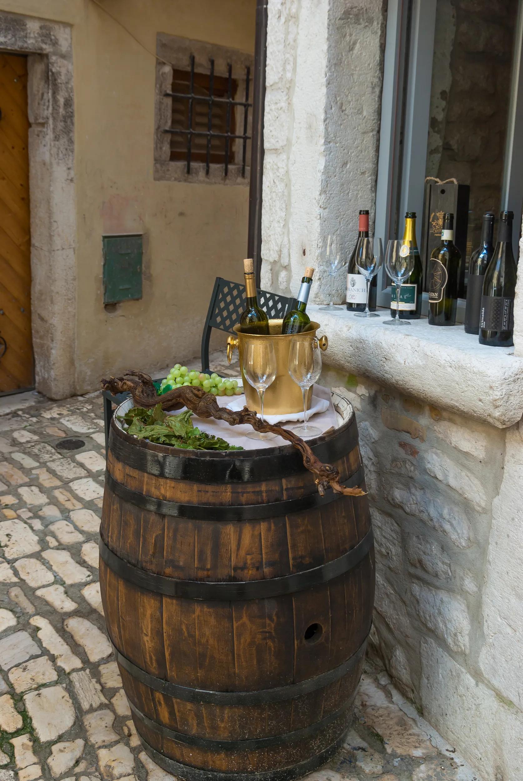 Rovinj,  Istria / Croatia, 2013 July  24, 2011: wine in an ice bucket, glasses, grapes, vine and leaves on a wooden barrel on a old city street. The liquor store expanded its display case onto the street.