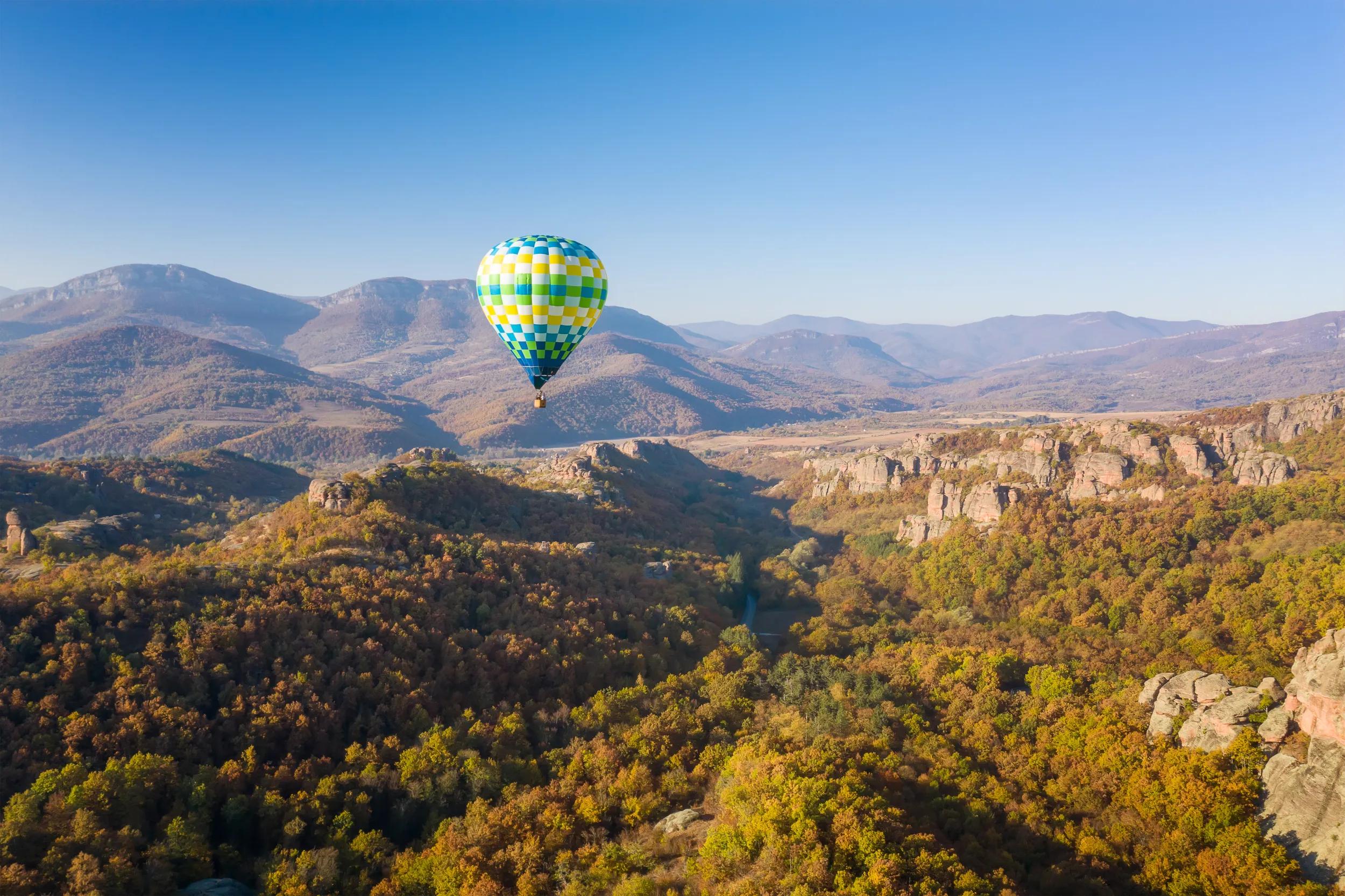 Amazing panoramic view with hot air balloon flying over picturesque rock formation lit by the morning autumn sun, Belogradchik rocks, Bulgaria