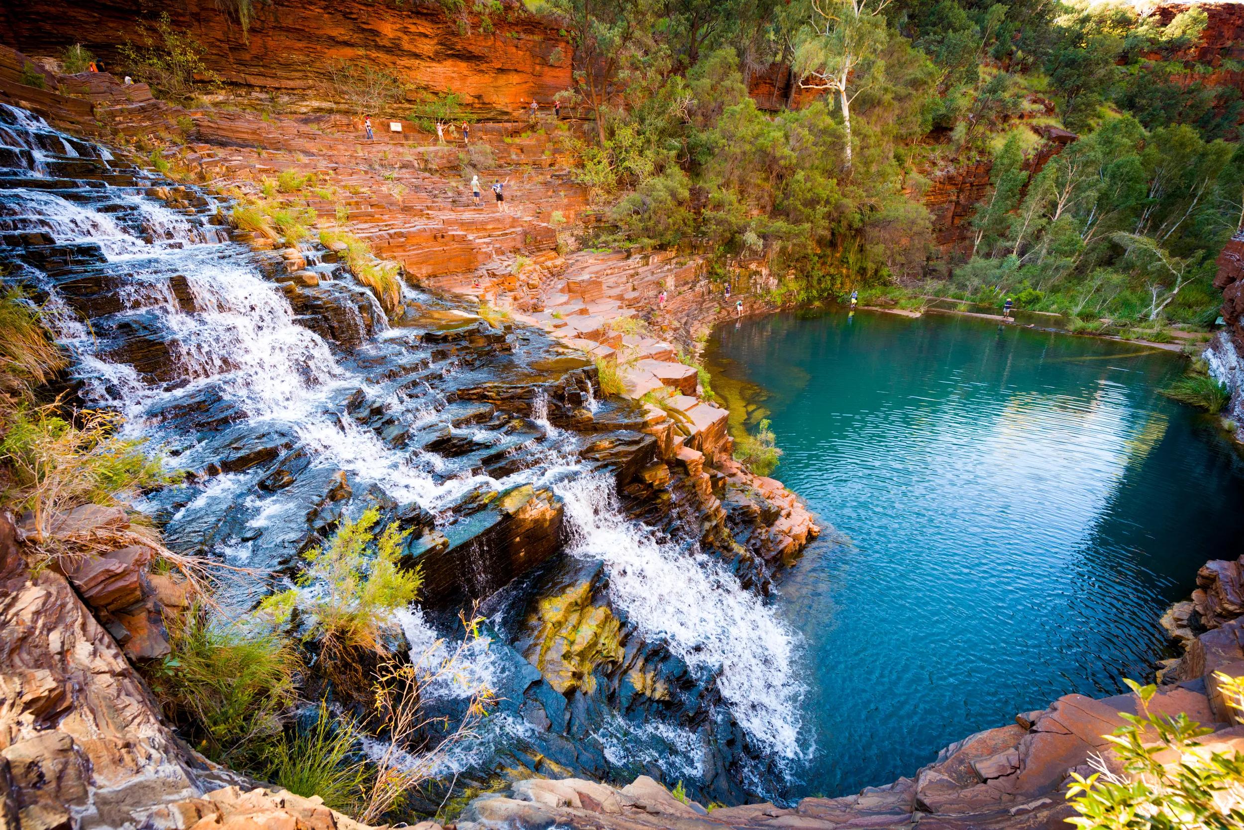 Water flowing over red rock into a pool.