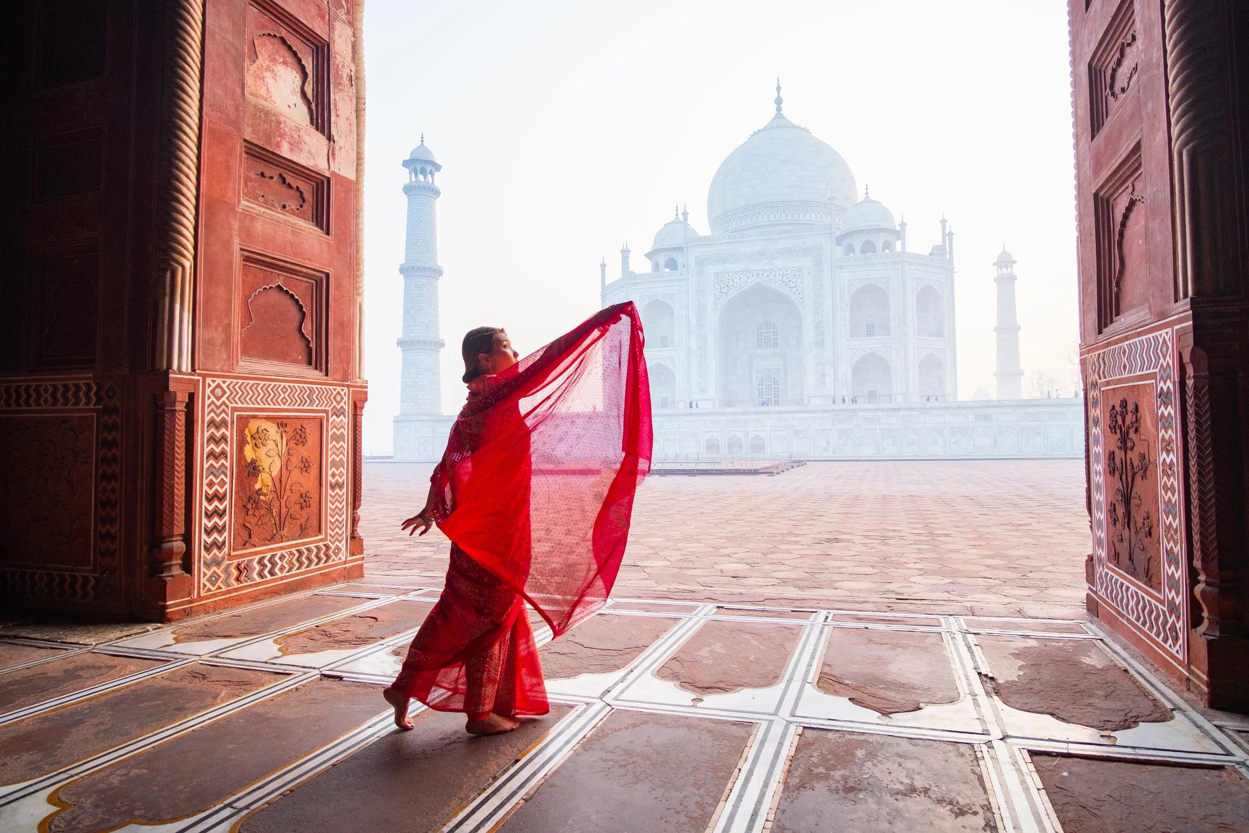An image of a young woman at the Taj Mahal in Agra, India, wearing a traditional red saree
