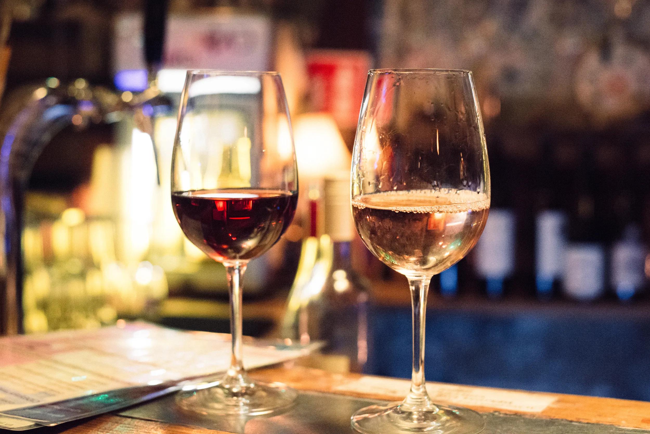 Glass of red wine standing next to glass of white wine close-up horizontal layout. Glass of red and white wine served and placed on bar stand in Szimpla Kert bar in Budapest Hungary.