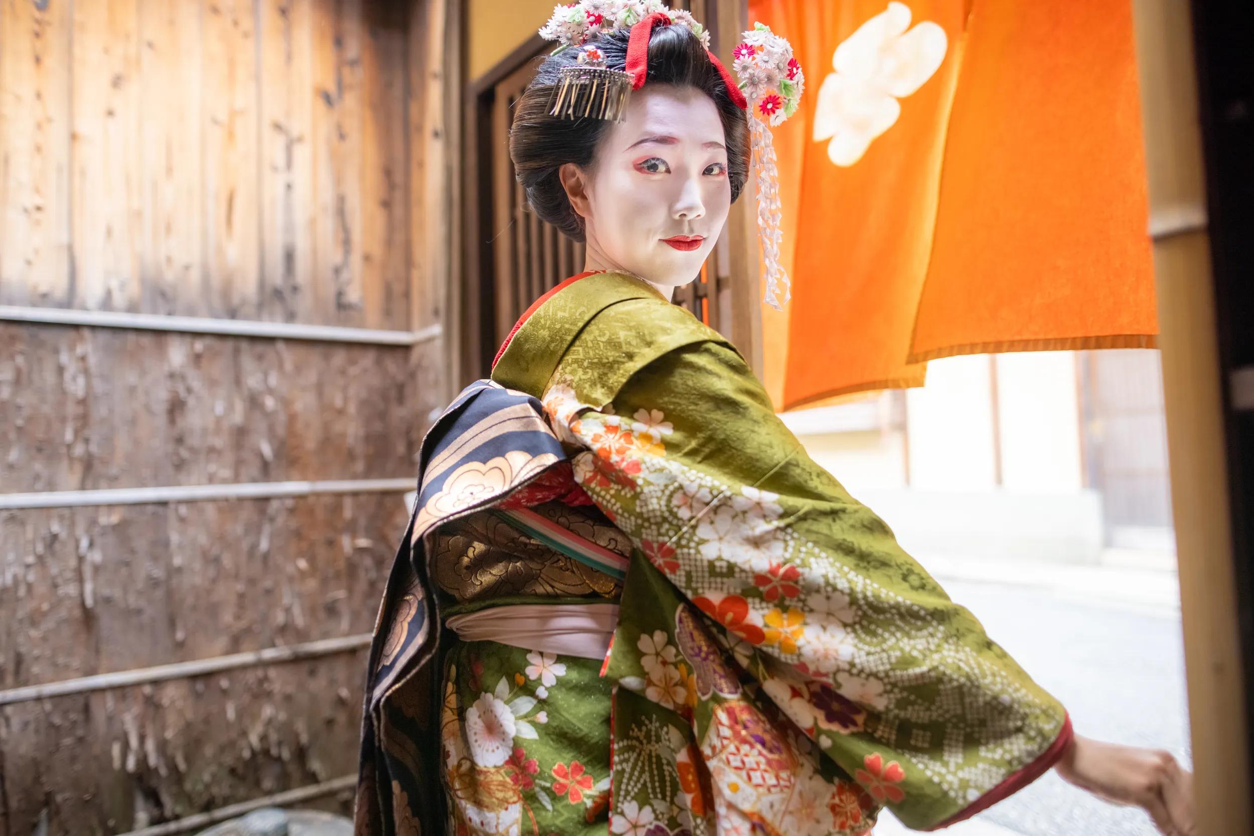 Young female tourist visiting Kyoto and experiencing Maiko (Geisha in training) makeover. Wearing traditional Japanese 'Maiko' style kimono with special white face makeup and walking around beautiful Gion district in Kyoto, Japan.