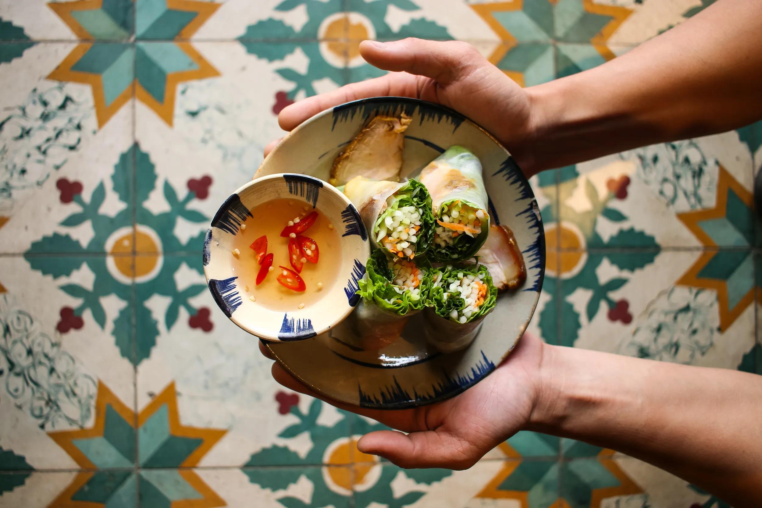 Directly above view of male hands holding a plate of leaf vegetable paper rolls with stewed pork served with nuoc cham dipping sauce