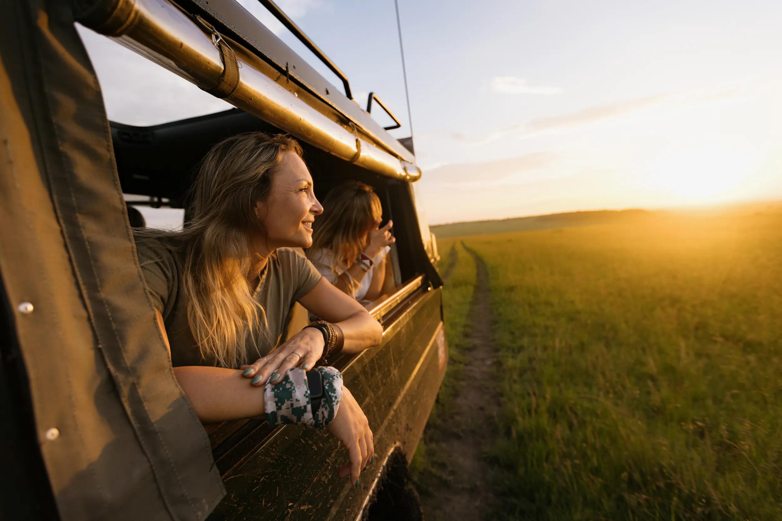 Happy woman riding in a jeep while enjoying in view of wildlife reserve at sunset.