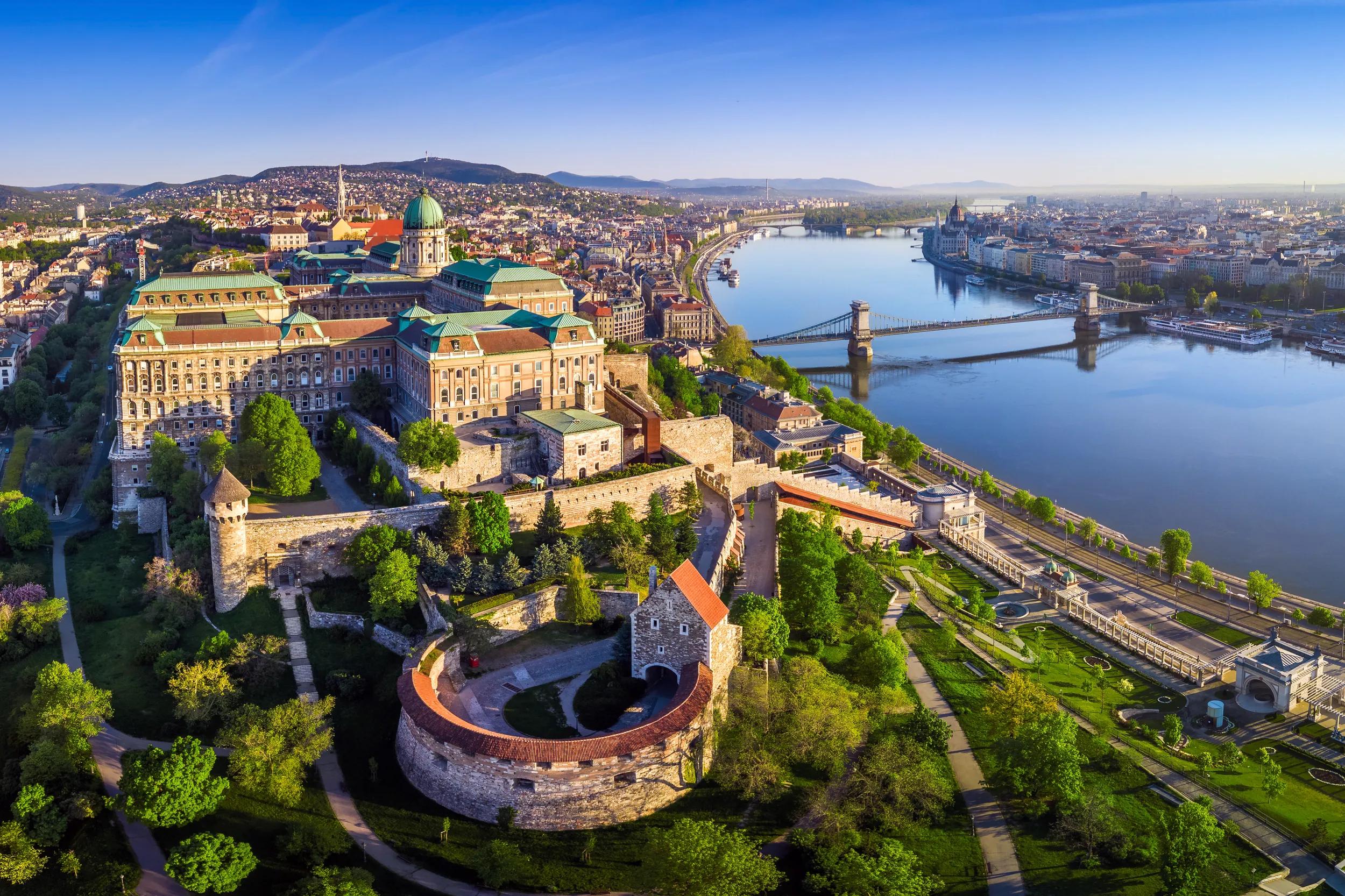 Aerial cityscape view of Buda Castle Royal Palace with Szechenyi Chain Bridge, Hungarian Parliament and Matthias Church at sunrise with clear blue sky, Budapest, Hungary.