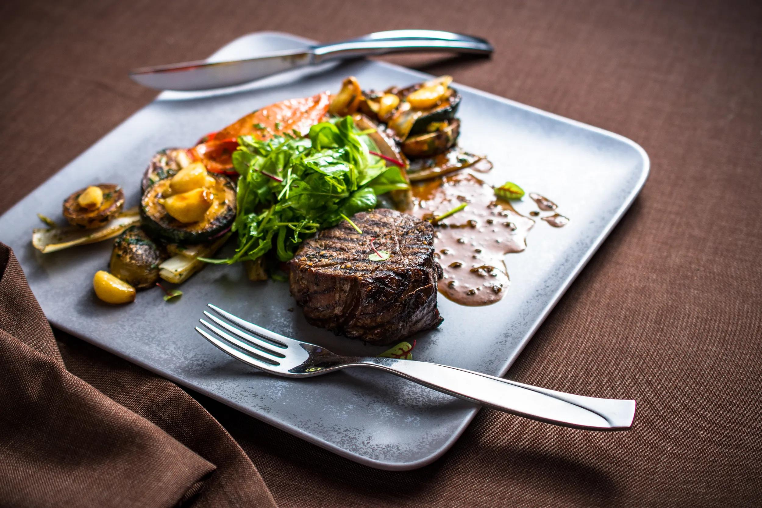 Grilled beef meat with grilled vegetables, gravy sauce and fresh green leaves
