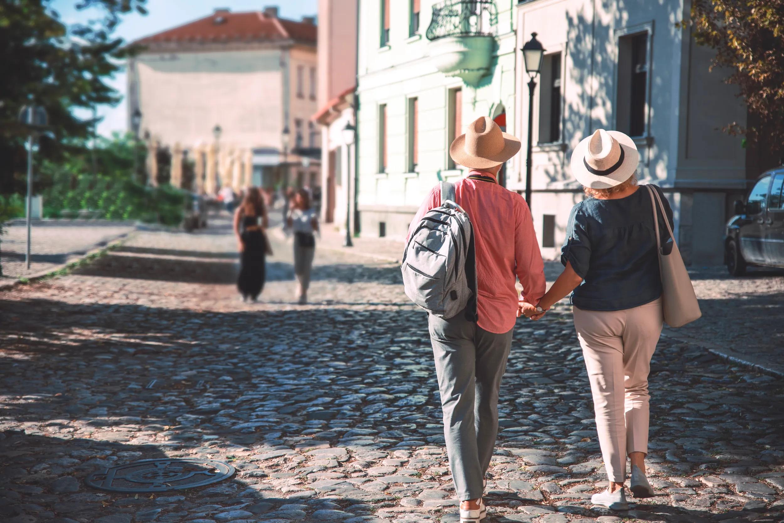 Back of Mature couple holding hands while walking in old town district. Copy space