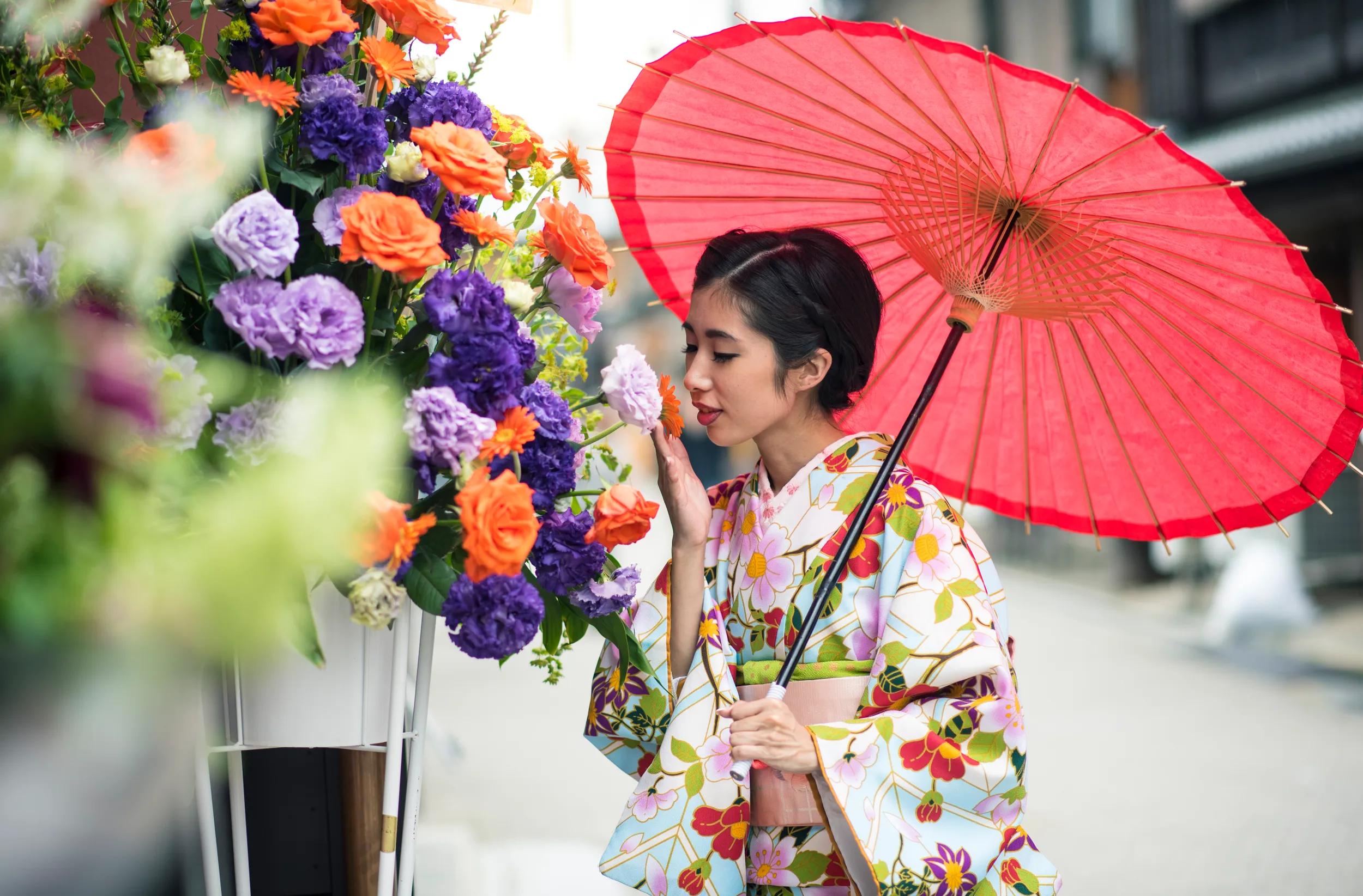 A young woman walking around Kyoto wearing a kimono, holding a red parasol