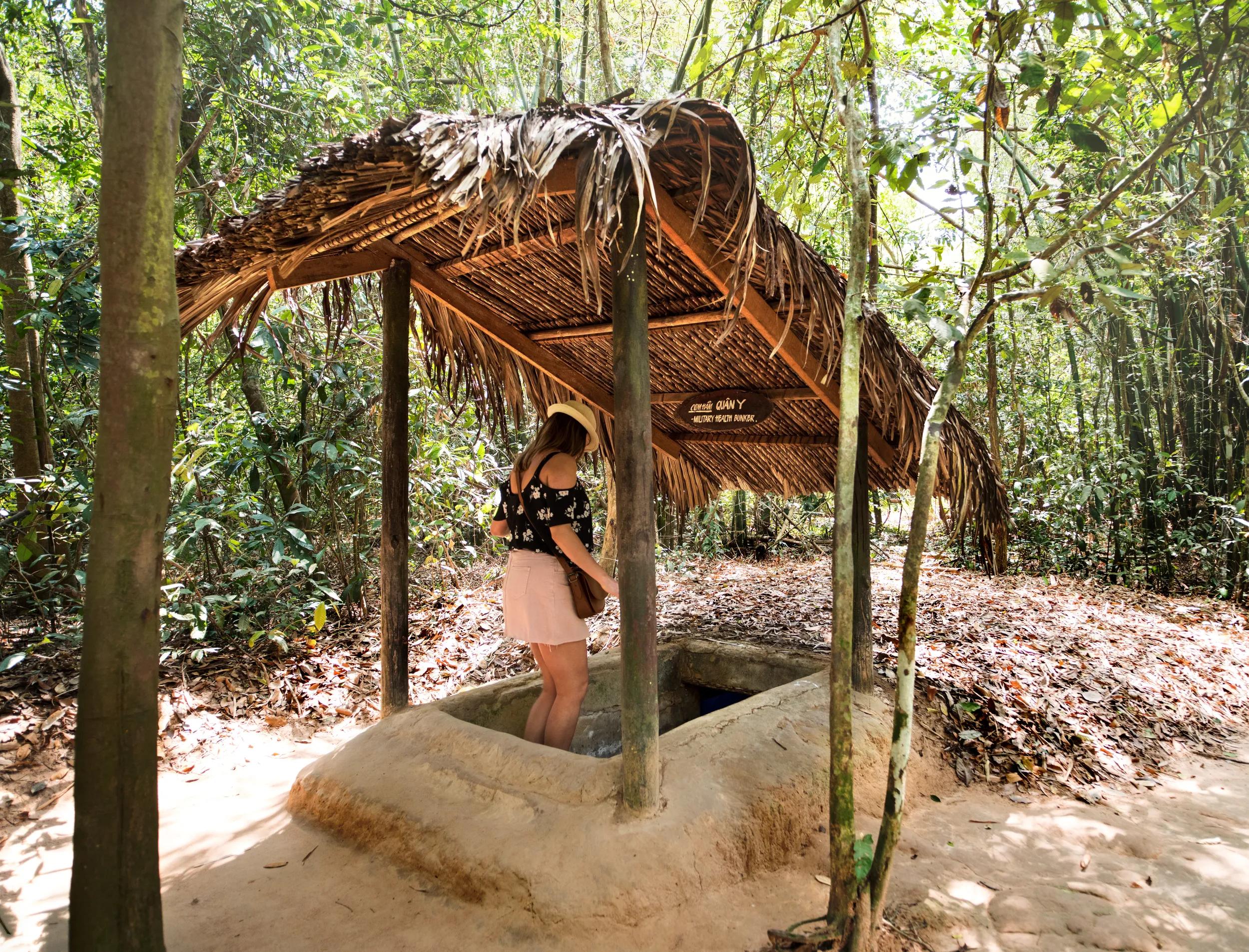 Famous Cu Chi tunnels. Tourist girl entering the tunnel.