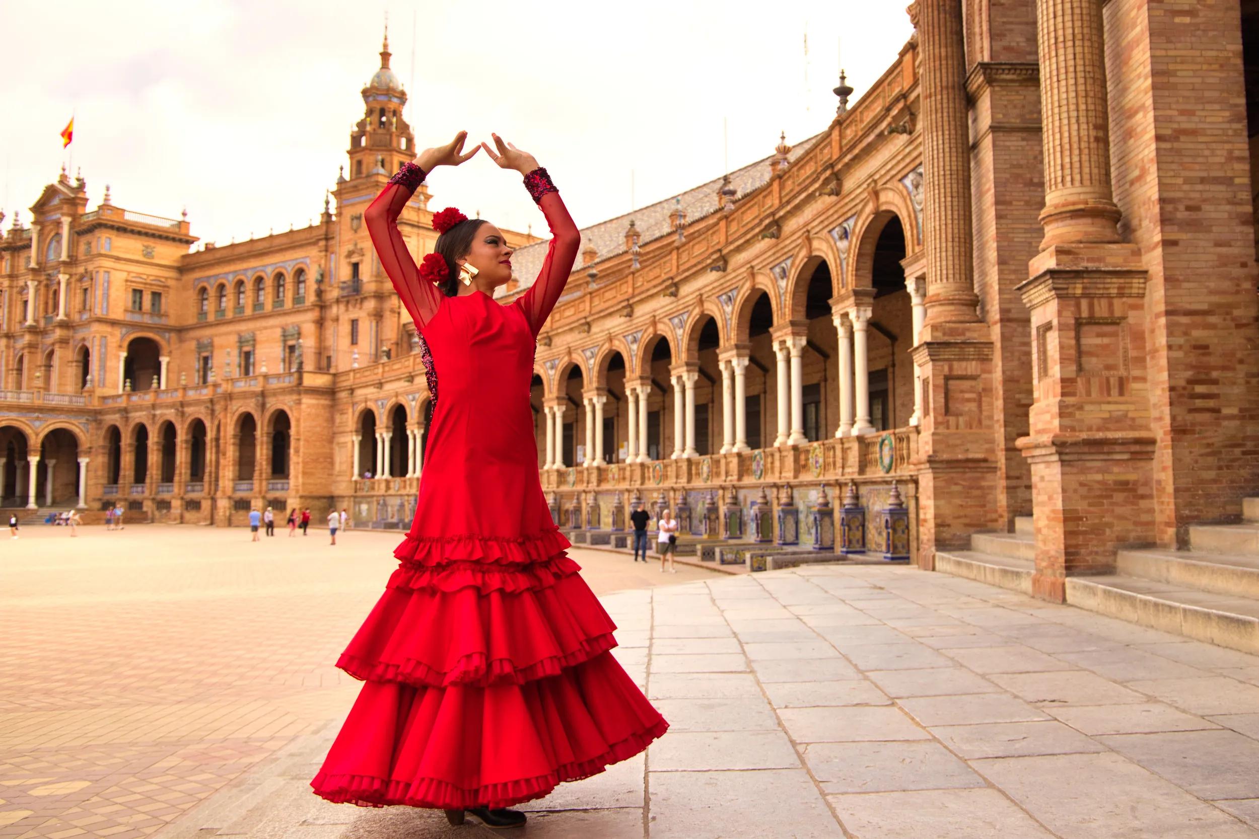 Beautiful teenage woman dancing flamenco in a square in Seville, Spain. She wears a red dress with ruffles and dances flamenco with a lot of art. Flamenco cultural heritage of humanity.