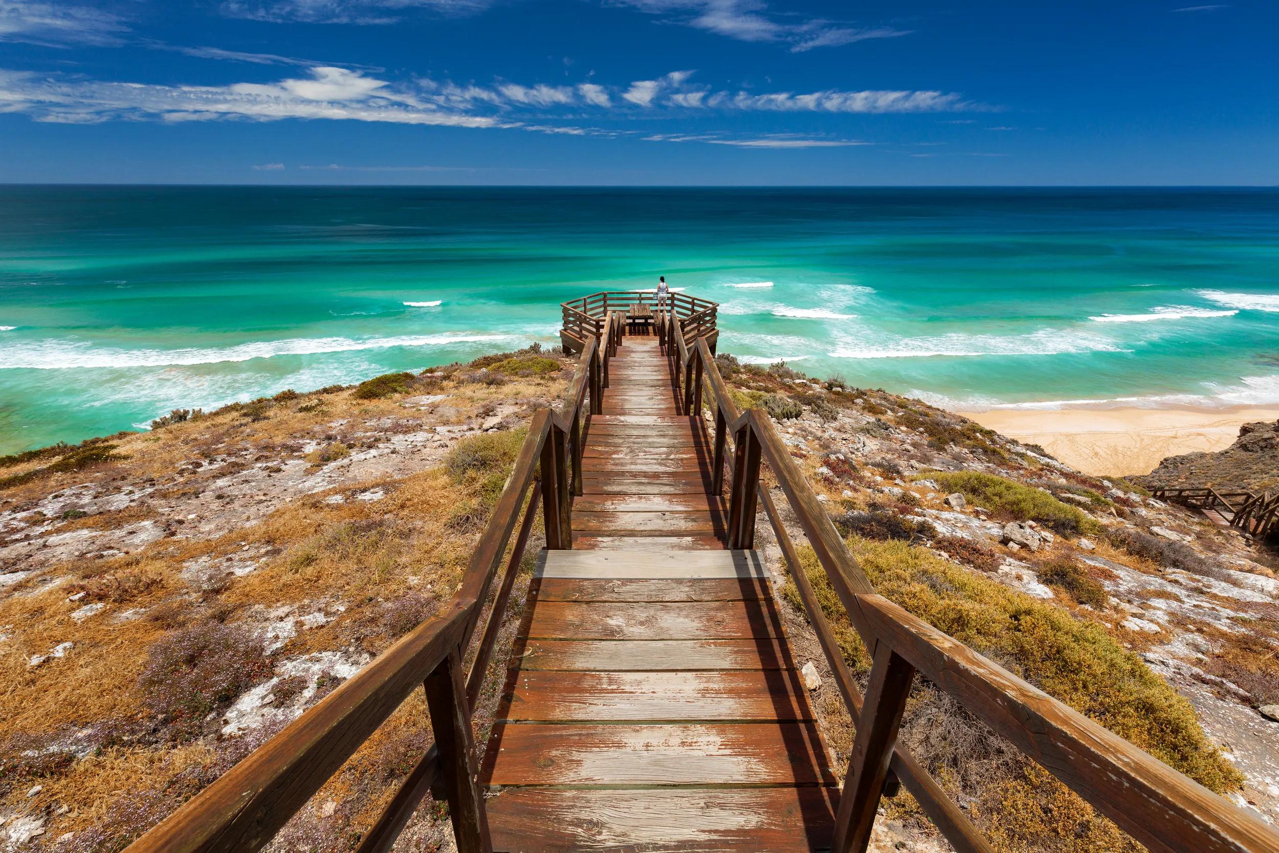 A lone woman stands at a lookout overlooking an ocean and beach