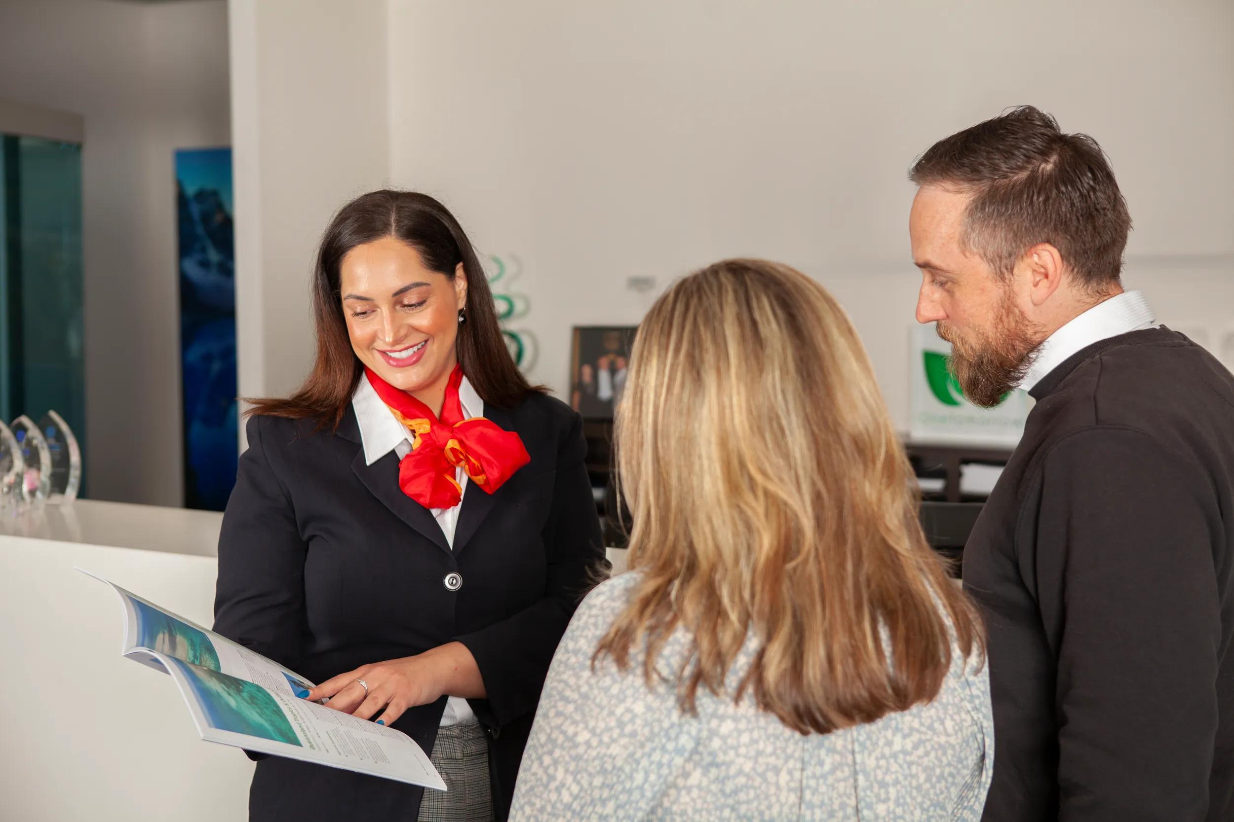 Tour Director showing clients a brochure in APT Head Office. Branding removed from background.