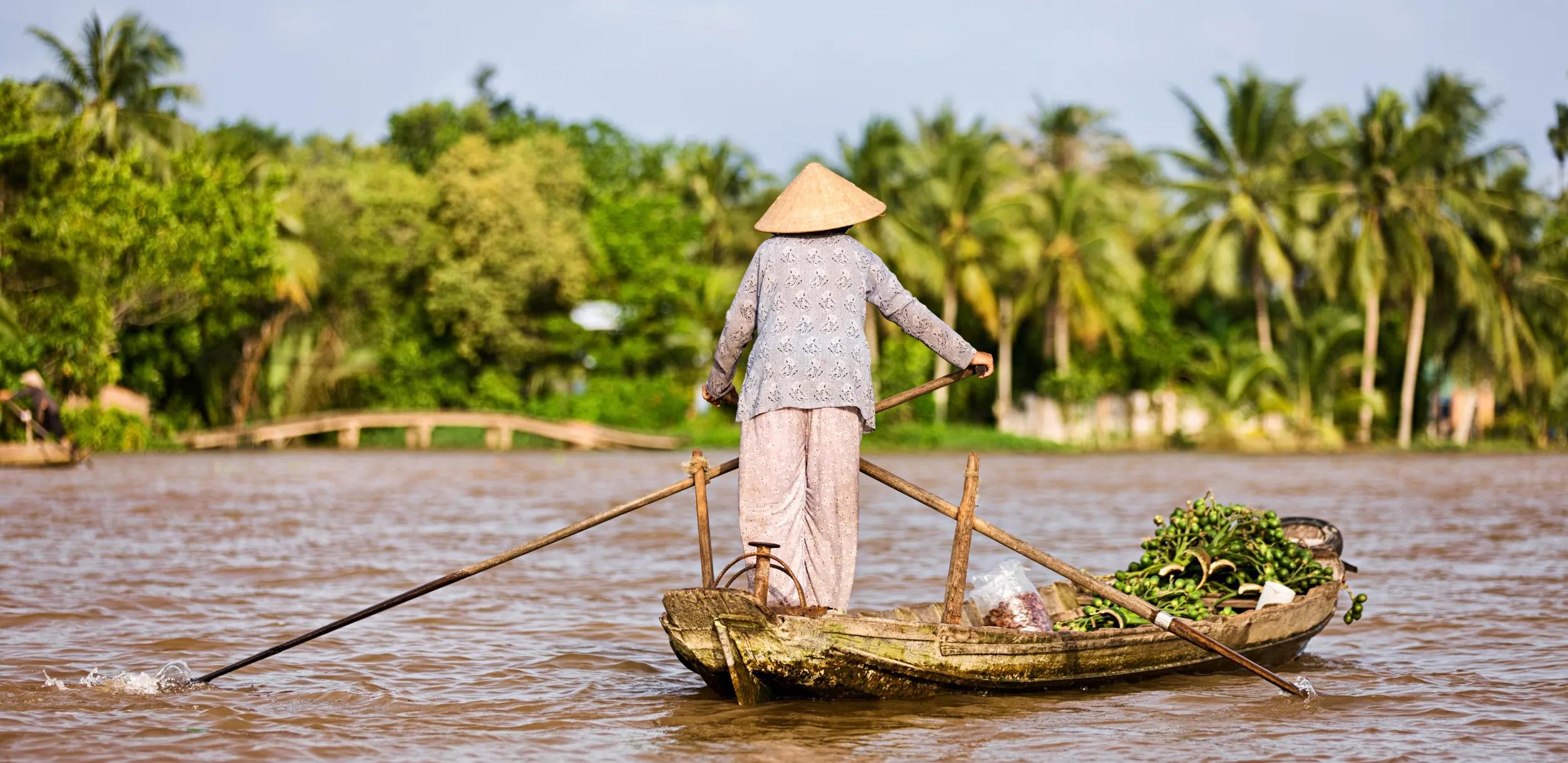 Vietnamese fruits seller - woman rowing boat in the Mekong river delta & selling fruits, Vietnam.