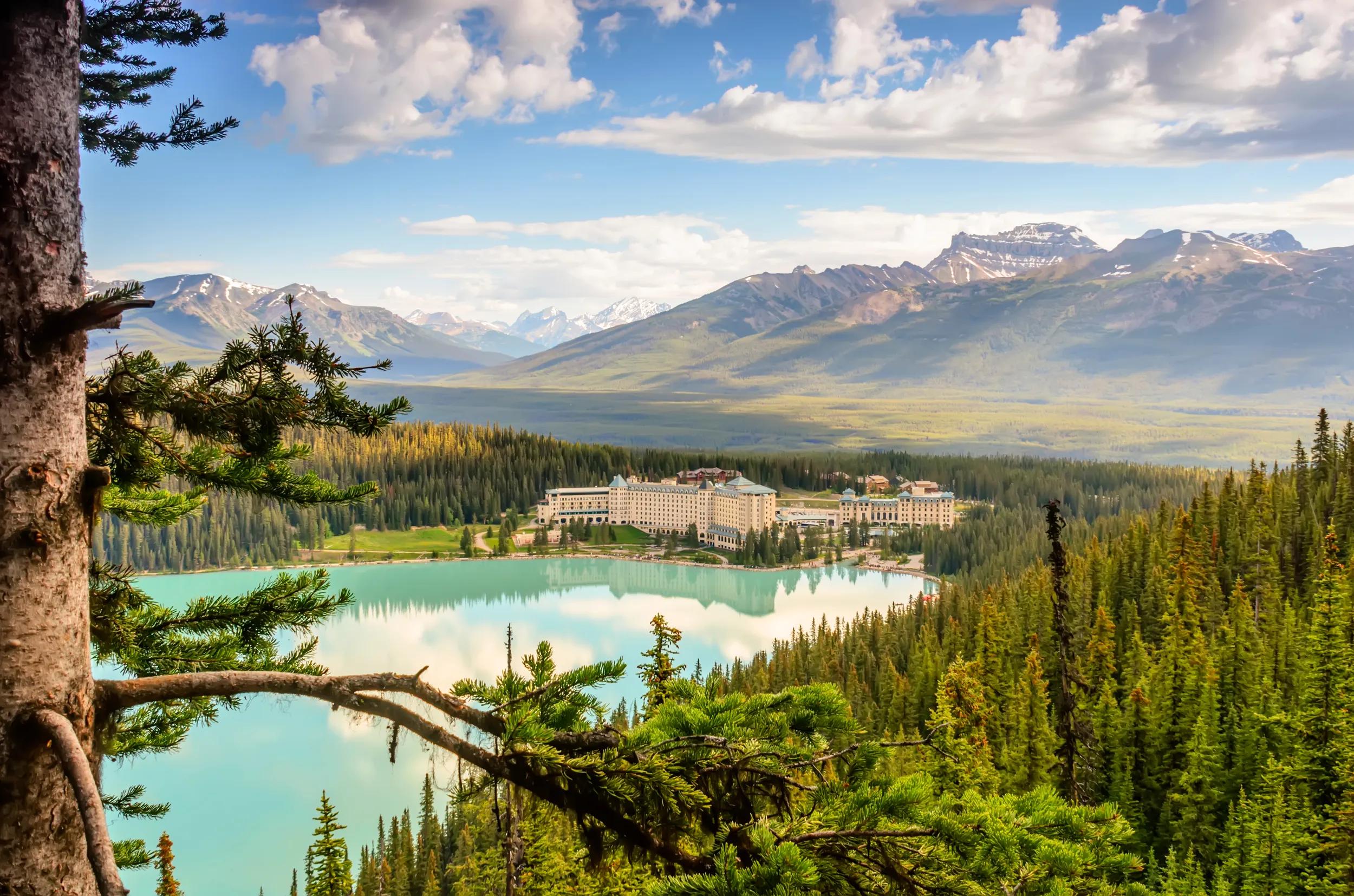 View of a blue lake and mountains from a height. Forest and buildings by the lake, blue sky with white clouds, on a summer day
