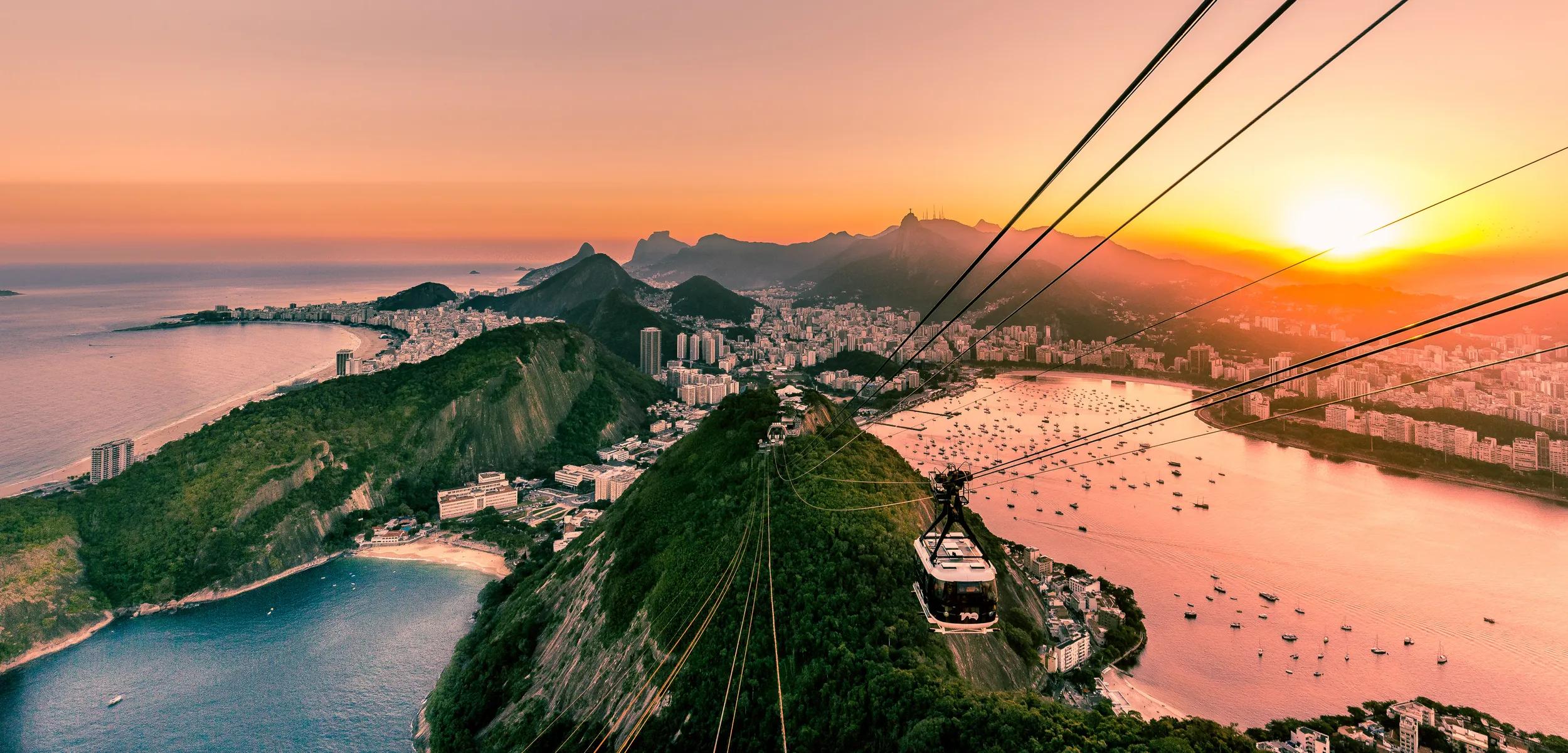 View from Sugarloaf mountain in Urca at sunset overlooking the city and mountains of Rio de Janeiro with cable car of tourists and boats in Guanabara bay down below in Rio, Brazil, South America