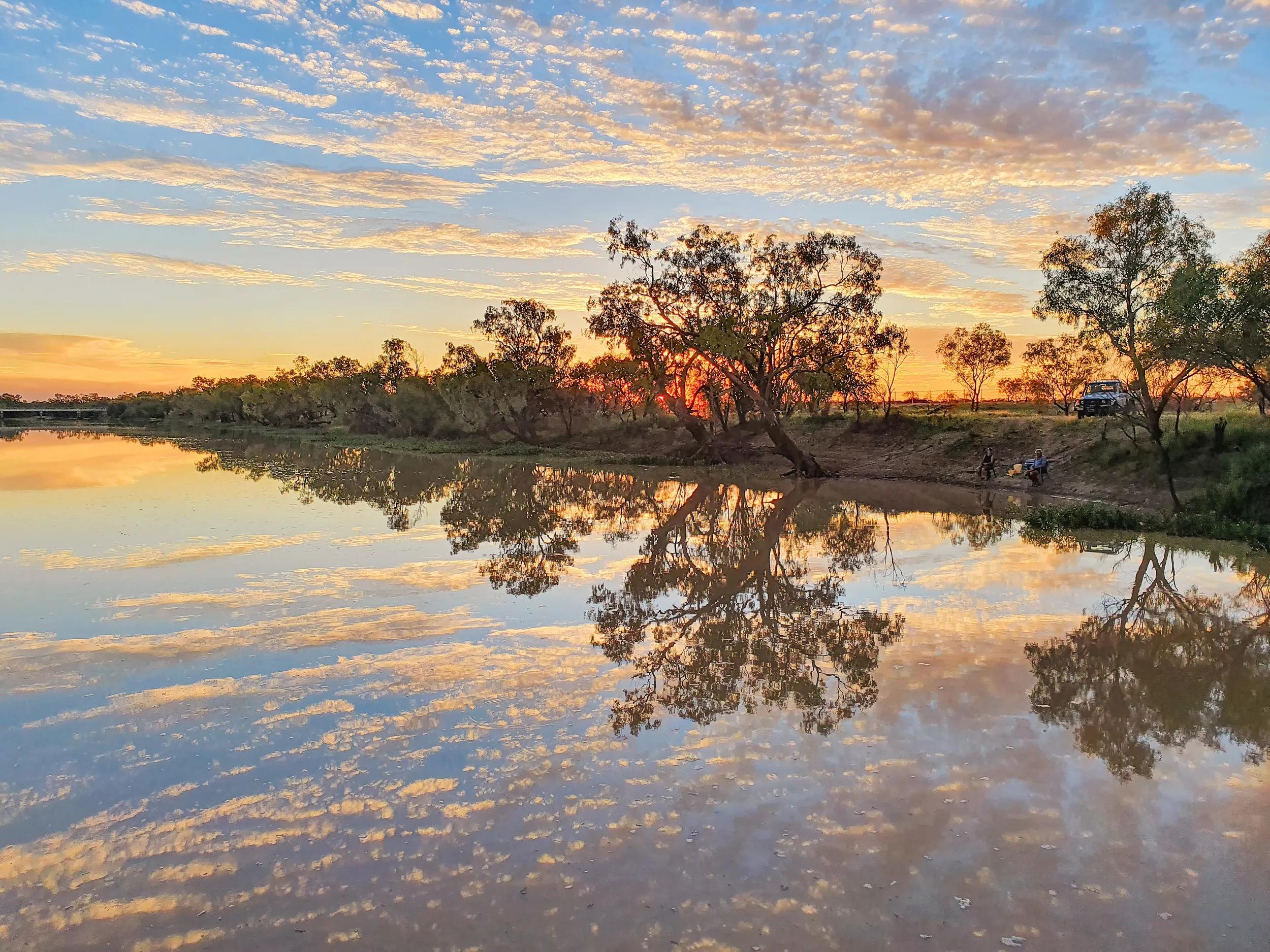 Sunset on the Thomson River at Longreach Queensland with people fishing on riverbank.