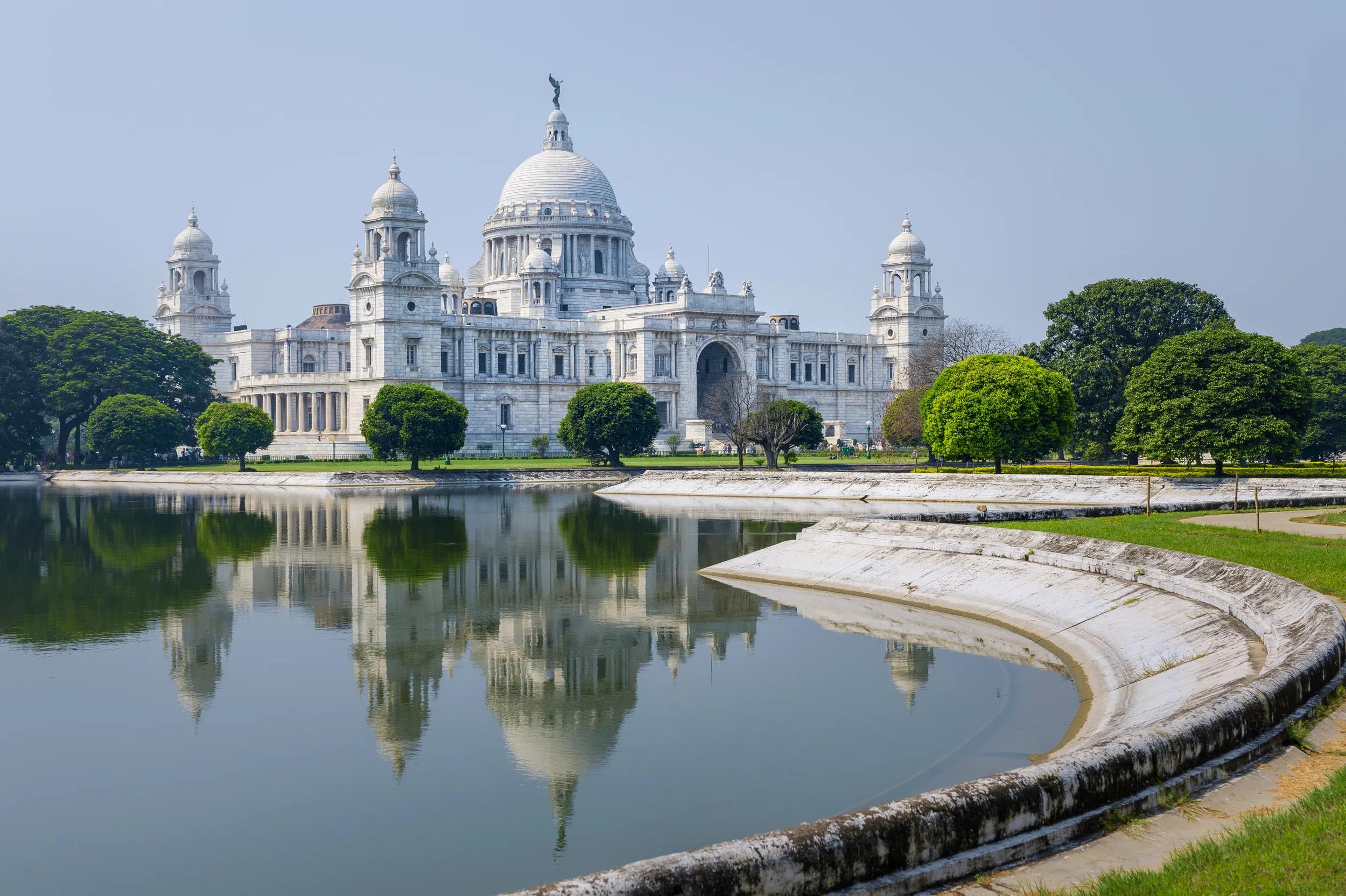 The Victoria Memorial, white marble monument in memory of Queen Victoria, on a bright sunny morning with blue sky with reflections of the memorial in the water feature to the front of the monument. Kolkata, India.