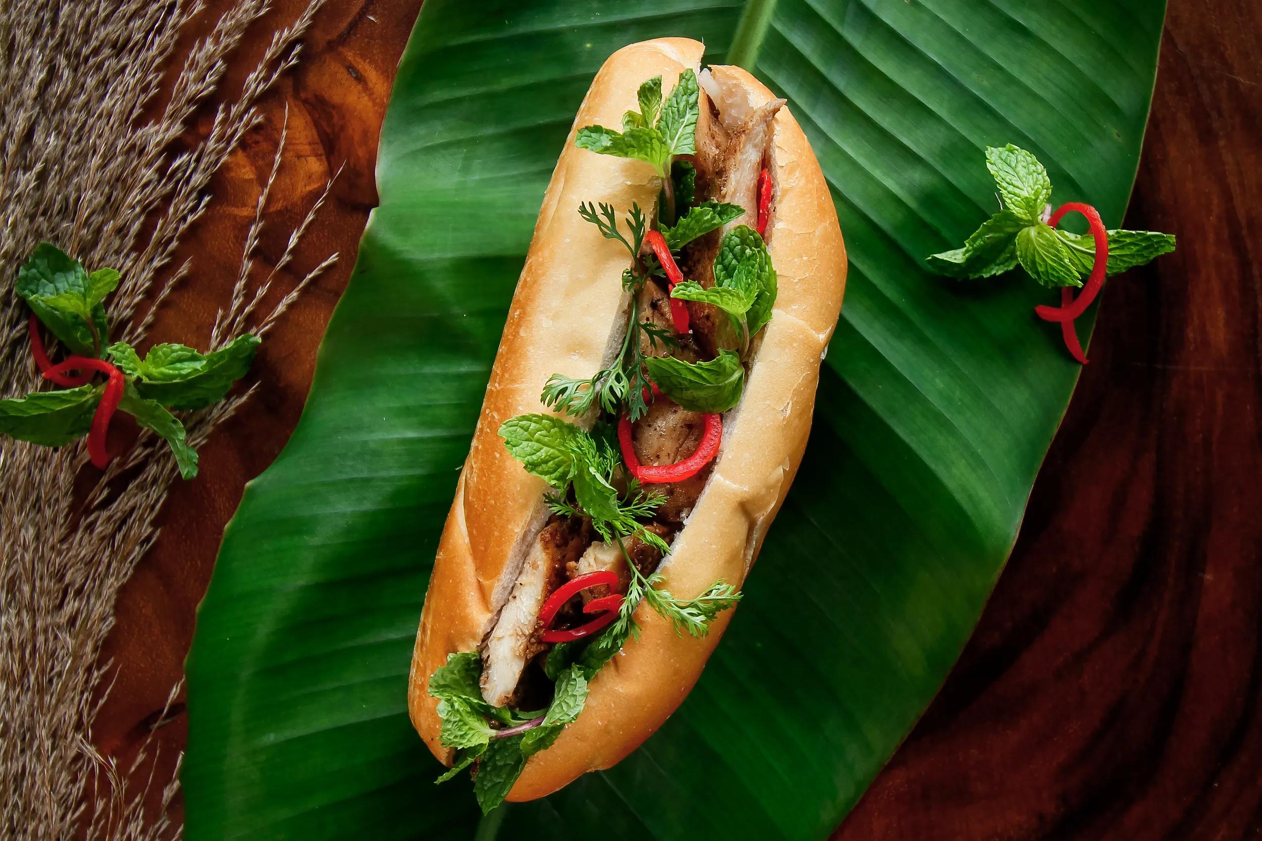 Overhead view of a Vietnamese Banh Mi roll stuffed with pork and mint leaves.